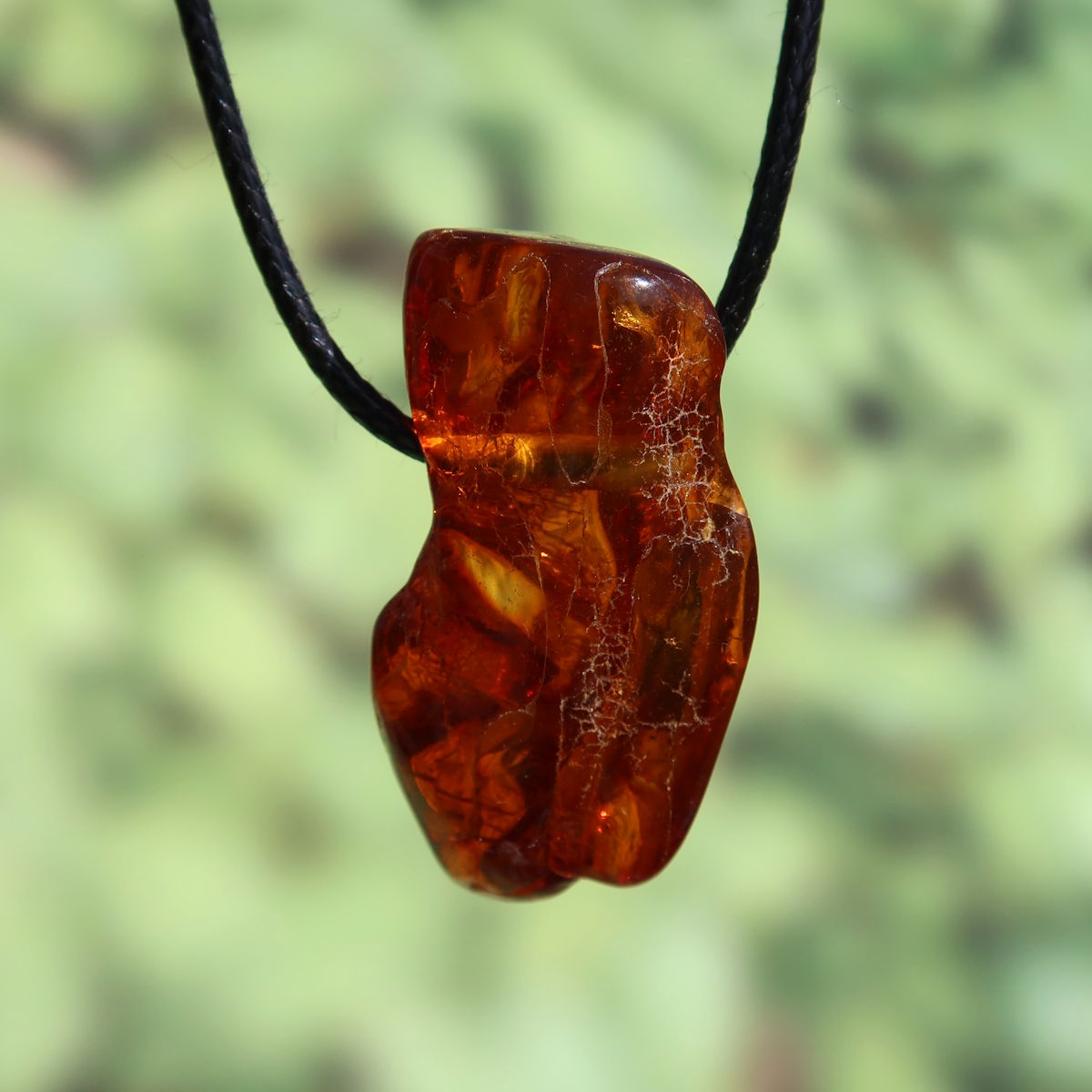 42mm natural amber pendant on black cord, unique design, shimmering with light, symbolizing vitality and self-confidence.