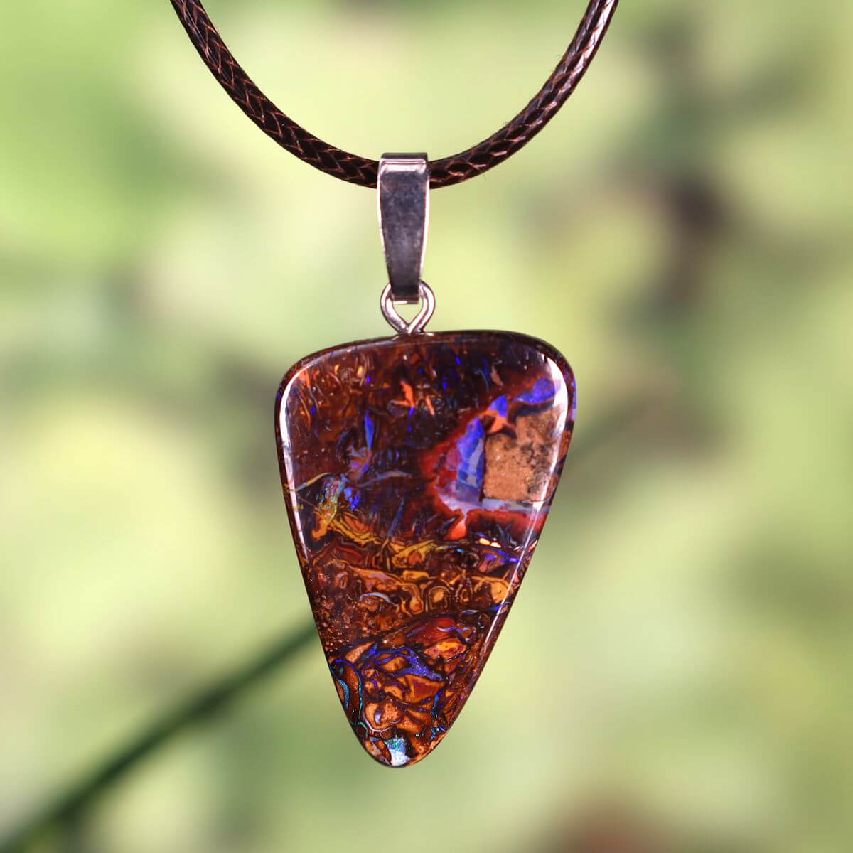 Boulder Opal pendant with rhodium silver loop, hand-polished gemstone, 33x23mm, unique from Australia, green blurred background.