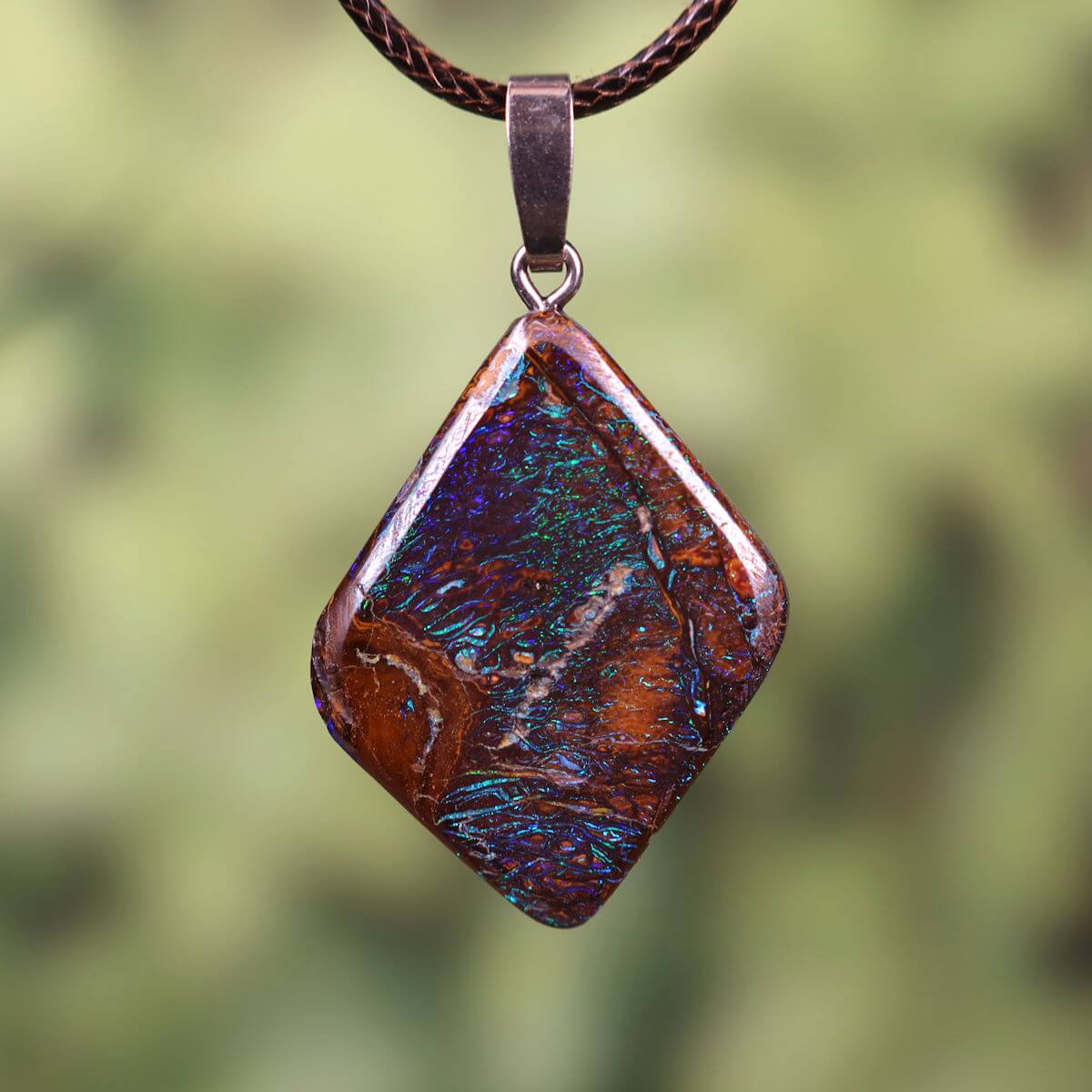 Handcrafted Boulder Opal pendant with rhodium-plated silver loop showcasing vibrant colors against a nature backdrop.
