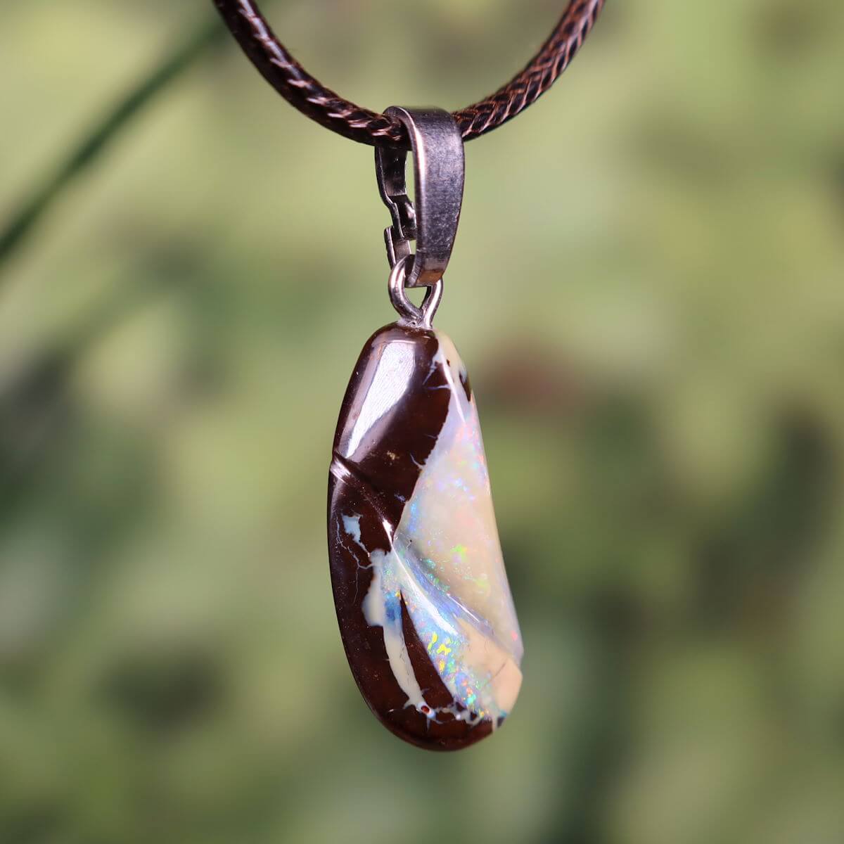 Unique Boulder Opal pendant with silver loop, hand-polished, 27x12mm size, displaying vibrant colors, hanging on a brown cord.