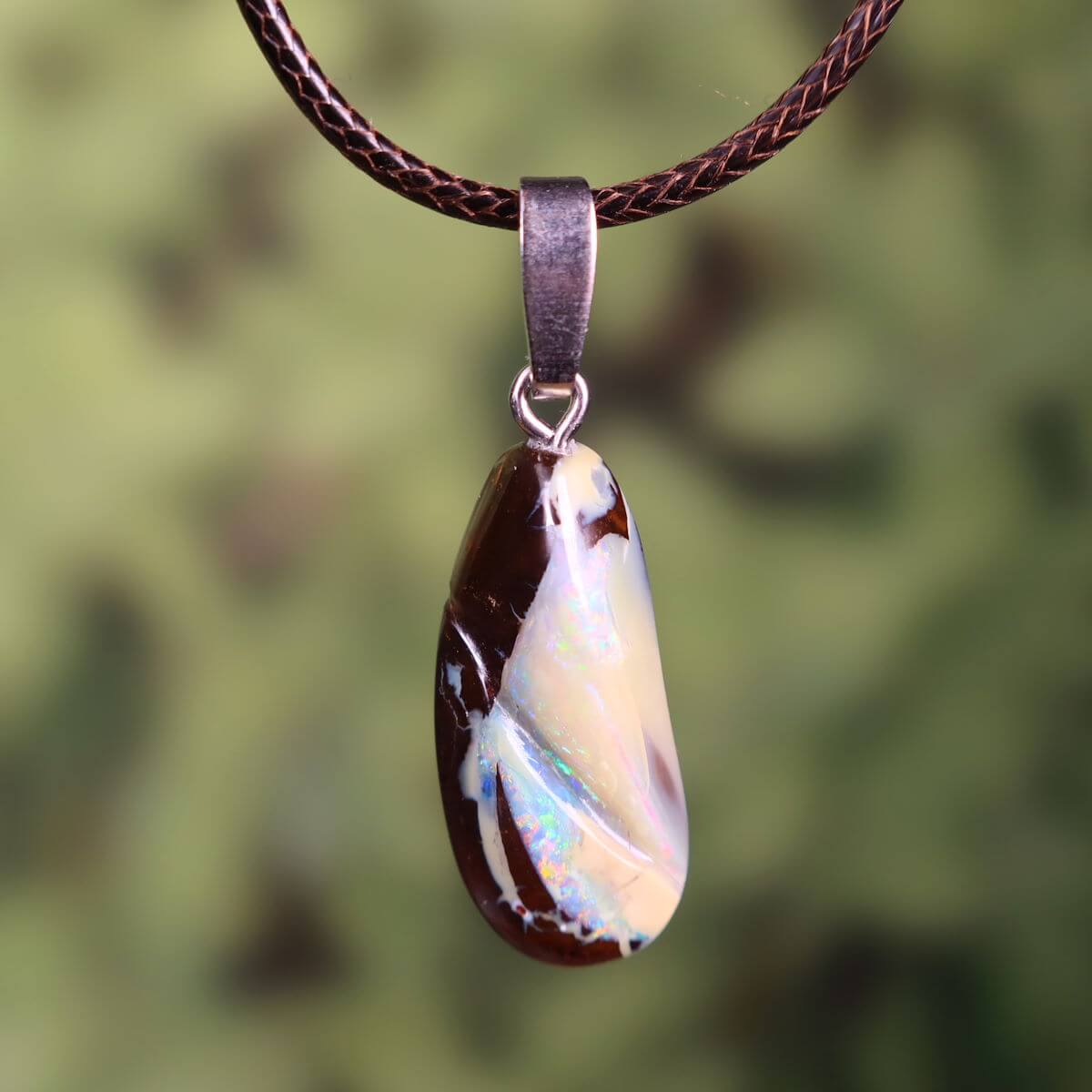 Unique Boulder Opal pendant with silver loop, hand-polished, 27x12mm size, displaying vibrant colors, hanging on a brown cord.