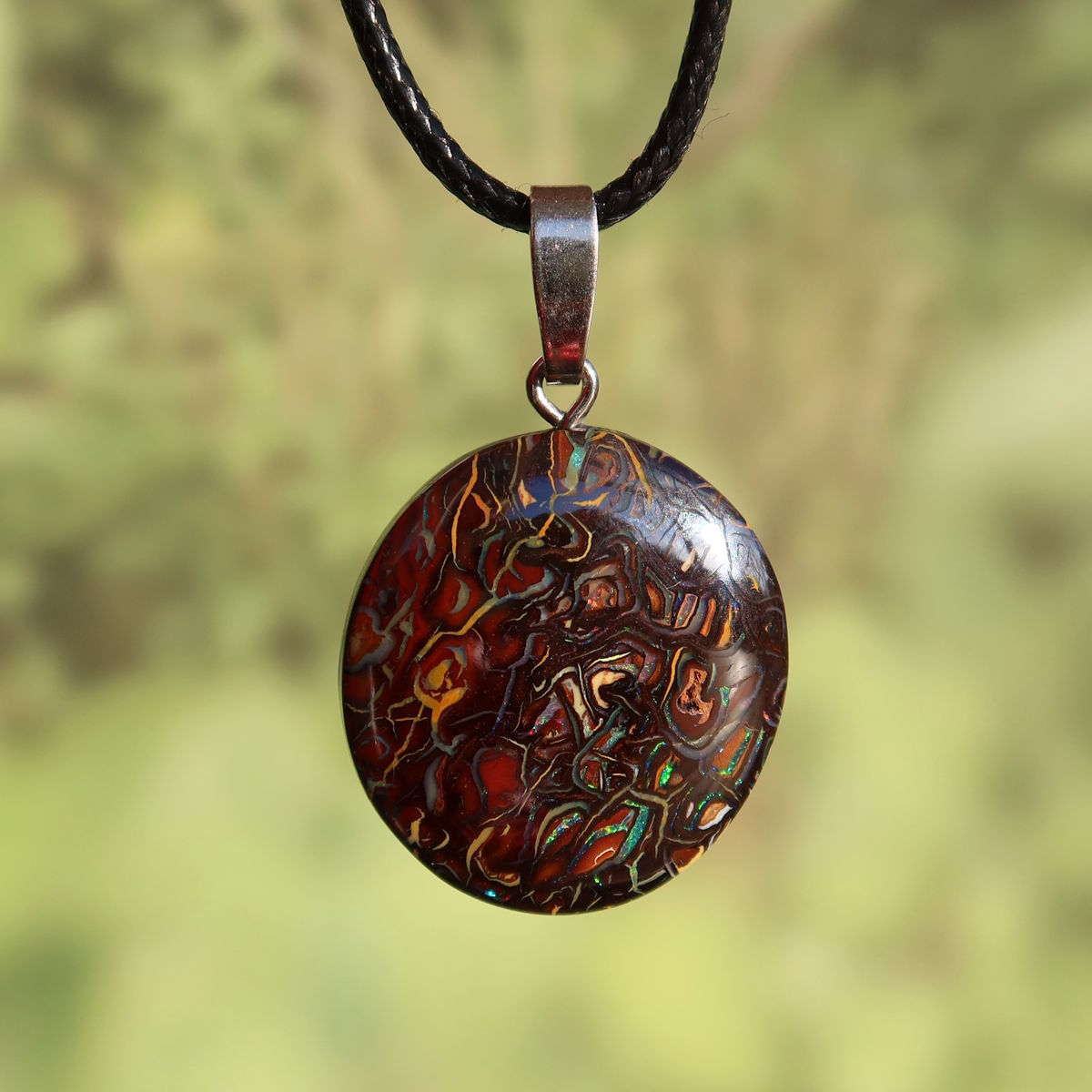 Boulder Opal Anhänger - Positivität und Freude - Nr. 12, einzigartiger Stein mit silberner Öse auf grünem Hintergrund.