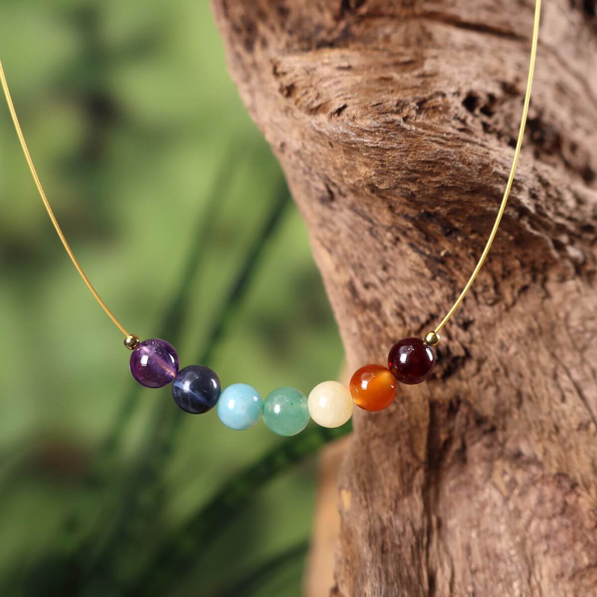 Chakra Edelsteinkette 40cm mit sieben farbigen Steinen für Balance und Ausgeglichenheit, elegant präsentiert auf Holz.