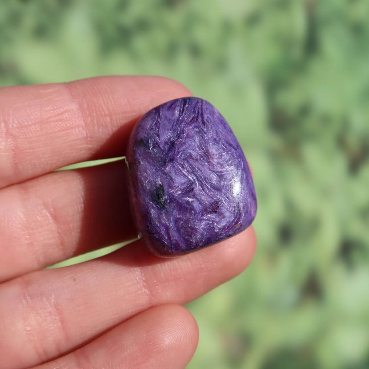 Violet Charoit Handschmeichler stone held by fingers, showcasing unique natural patterns, available for purchase online, Graz, Wiener Neustadt.