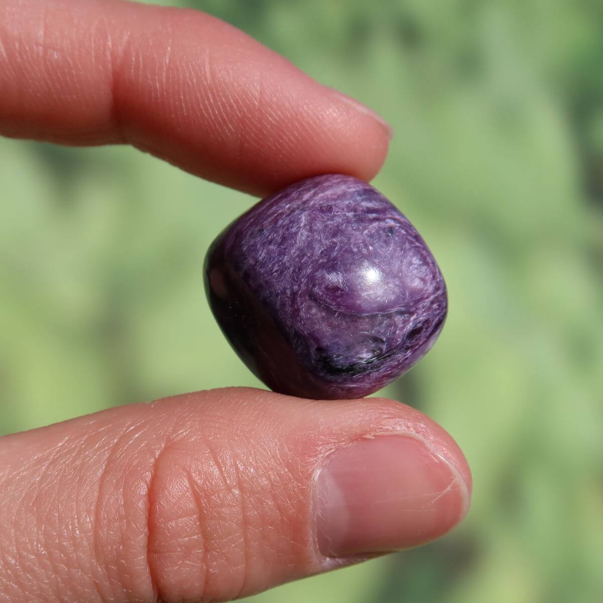 Hand holding a deep violet Charoit stone, highlighting its unique patterns and high quality, available to buy online in Graz and Wiener Neustadt.