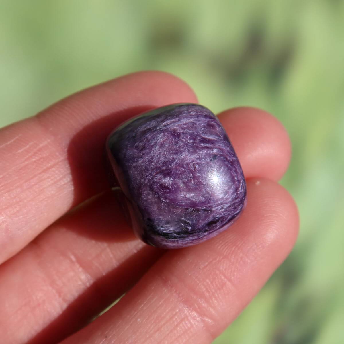 Hand holding a deep violet Charoit stone, highlighting its unique patterns and high quality, available to buy online in Graz and Wiener Neustadt.