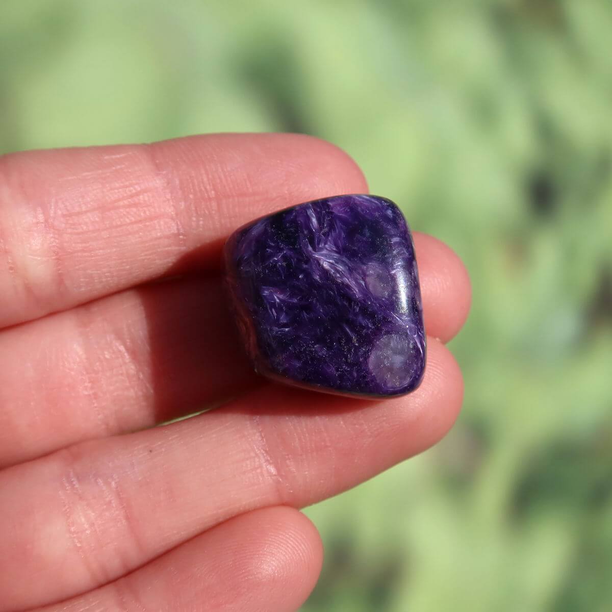 Hand holding a deep violet Charoit stone, available online, unique gemstone with distinctive patterns, ideal for jewelry making.