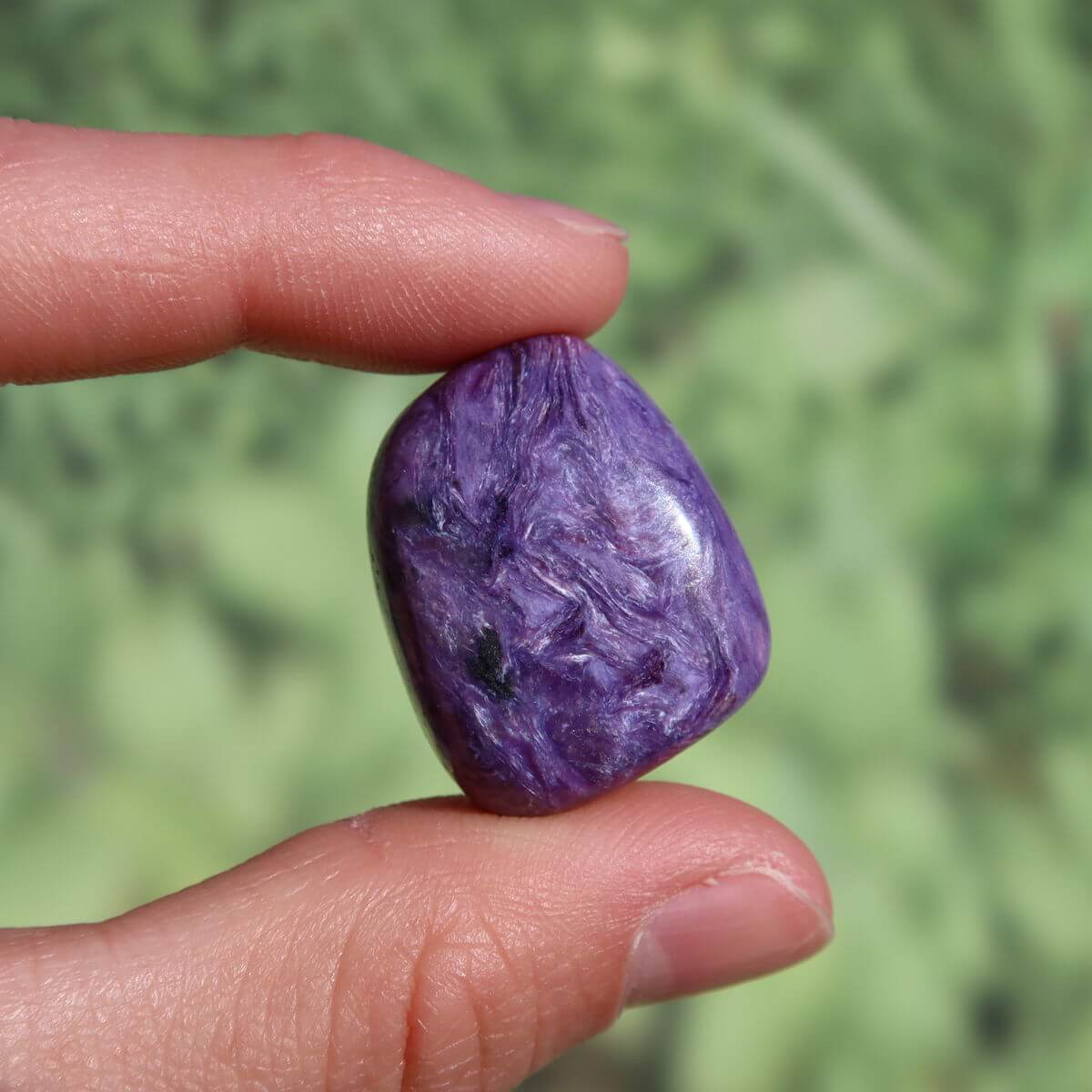 Violet Charoit Handschmeichler stone held by fingers, showcasing unique natural patterns, available for purchase online, Graz, Wiener Neustadt.