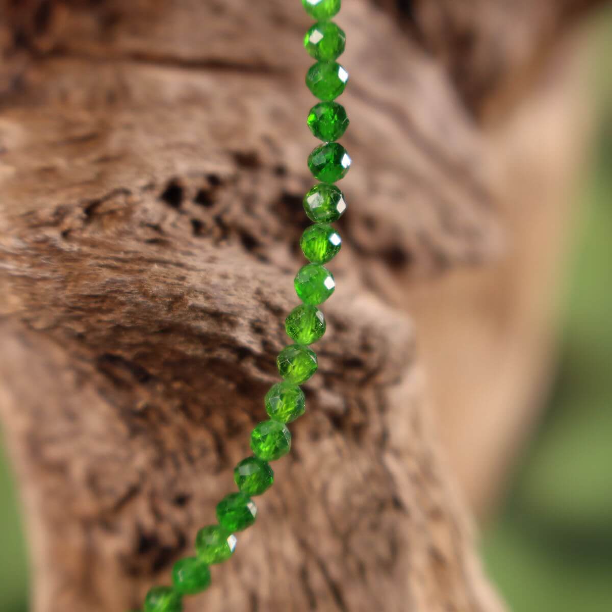 Handcrafted chromdiopside necklace with vivid green gemstones and silver rhodium-plated elements displayed on driftwood background.