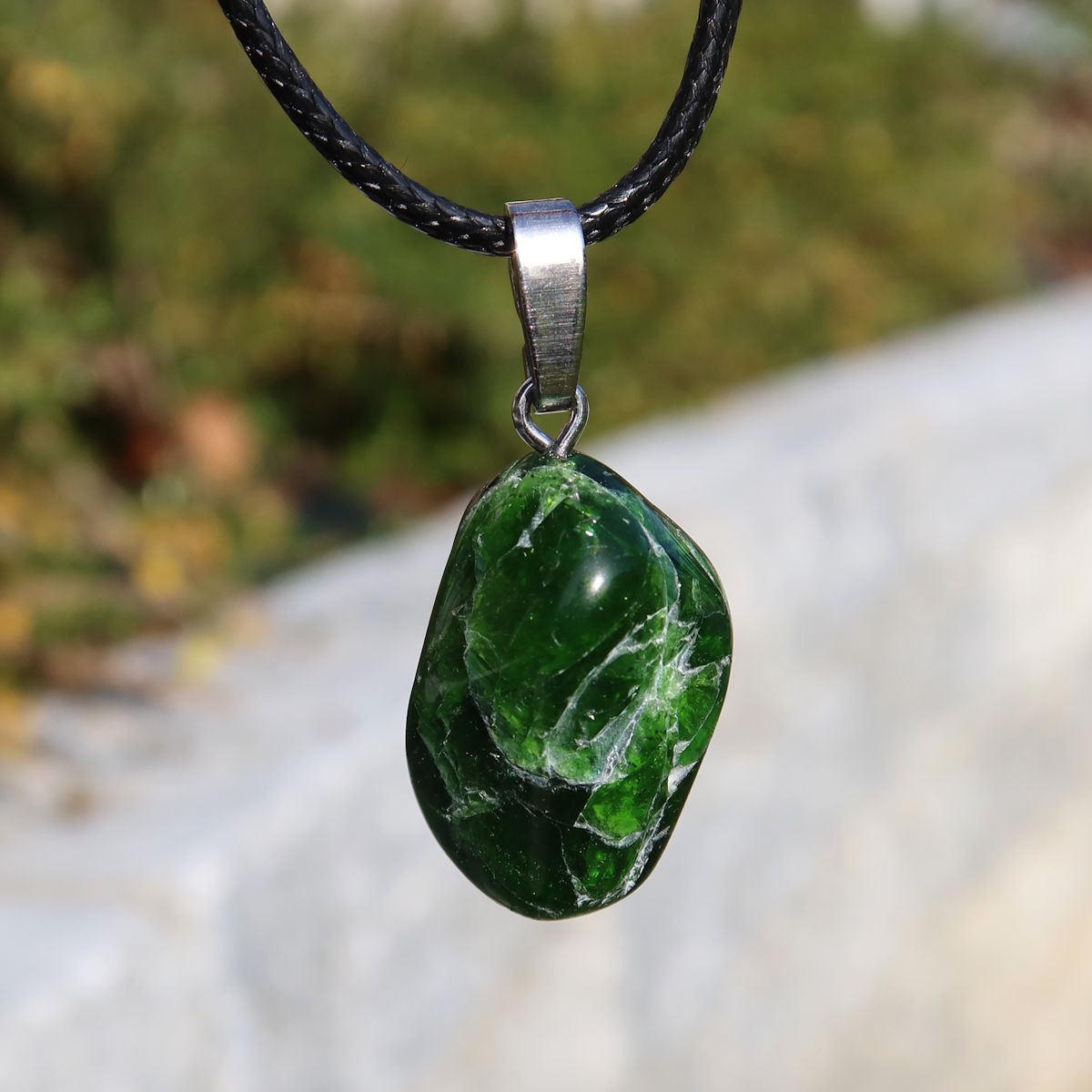 Natürlicher Chromdiopsid Anhänger 24mm - Kreativität und Leichtigkeit - UNIKAT Nr. 13, grüner Edelstein an schwarzer Kette im Sonnenlicht.