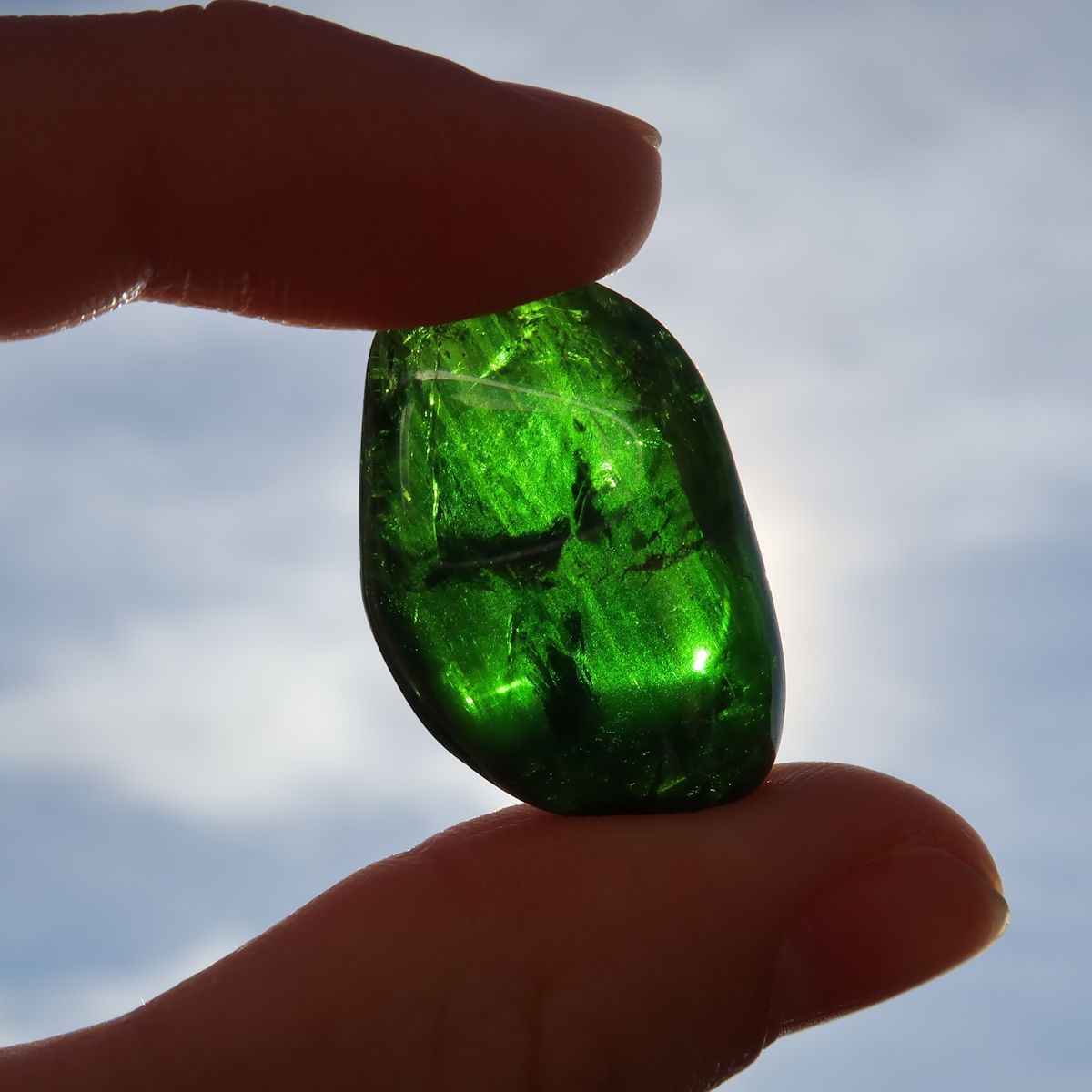 Natürlicher Chromdiopsid Handschmeichler 26mm - Kreativität und Leichtigkeit - UNIKAT Nr. 4 in der Hand gehalten, vor Himmelshintergrund