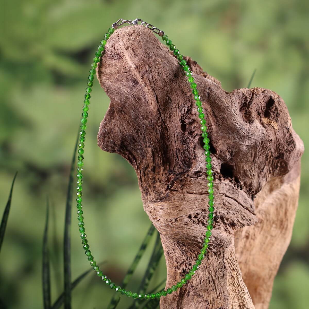 Handcrafted chromdiopside necklace with vivid green gemstones and silver rhodium-plated elements displayed on driftwood background.