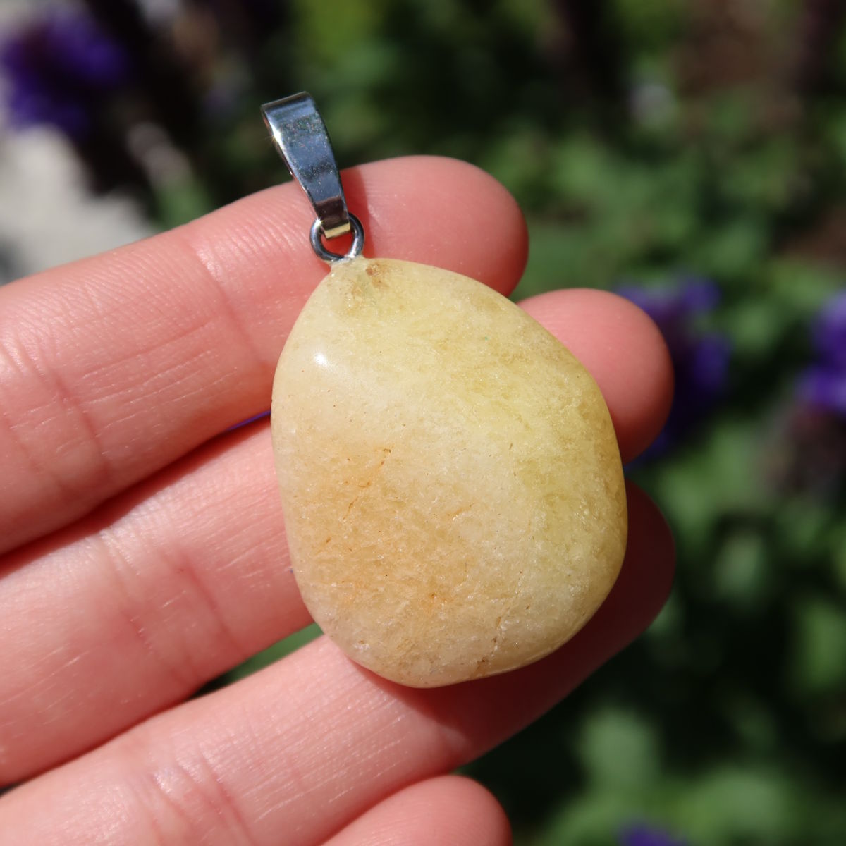 Yellow Danburit pendant in hand, unique gemstone with sunny hue, showcases clear structure and fine color nuances, nature background.