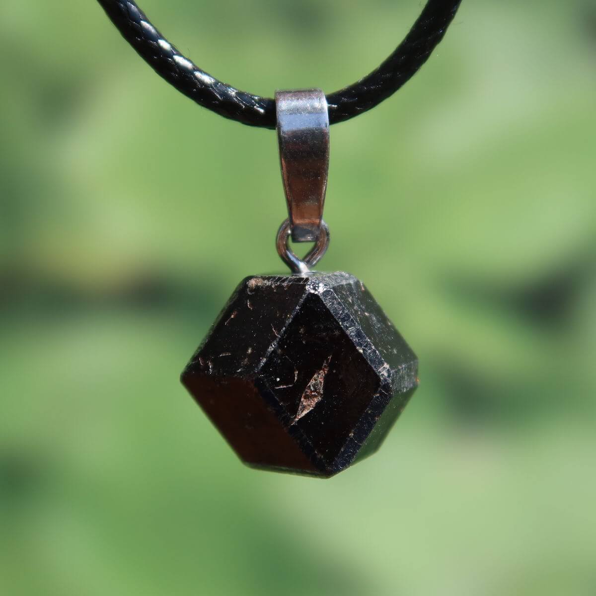 Natürlicher Granat Melanit Anhänger - Standfestigkeit und Stabilität - UNIKAT Nr. 10 in tiefschwarzem Glanz vor grünem Hintergrund.