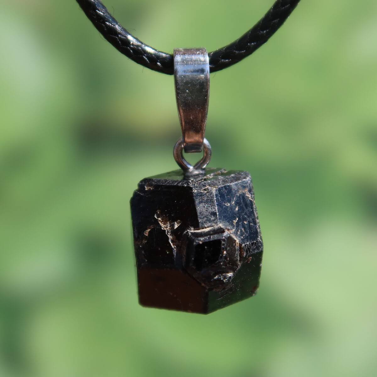 Natürlicher Granat Melanit Anhänger - Standfestigkeit und Stabilität - UNIKAT Nr. 3, glänzender schwarzer Edelstein auf grüner Kulisse