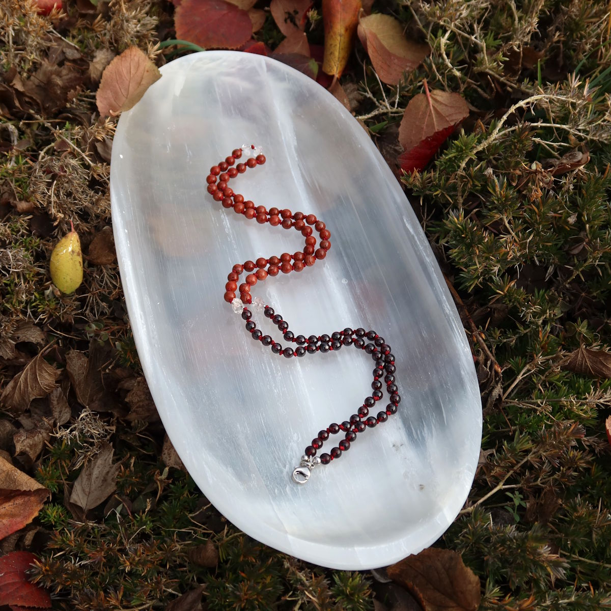 Handgemachte Mala Kette aus Granat und Jaspis auf weißem Teller, symbolisiert Erdung und Stabilität, Kategorie Nr. 24.