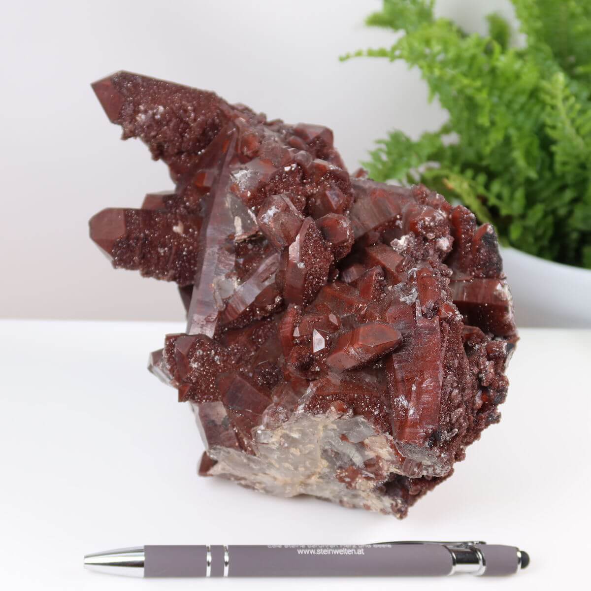 Seltene Hämatit Quarz Bergkristall aus Marokko, Eisenquarz Stufe mit intensiver Farbe, auf Tisch neben Stift, Steinwelten online kaufen.