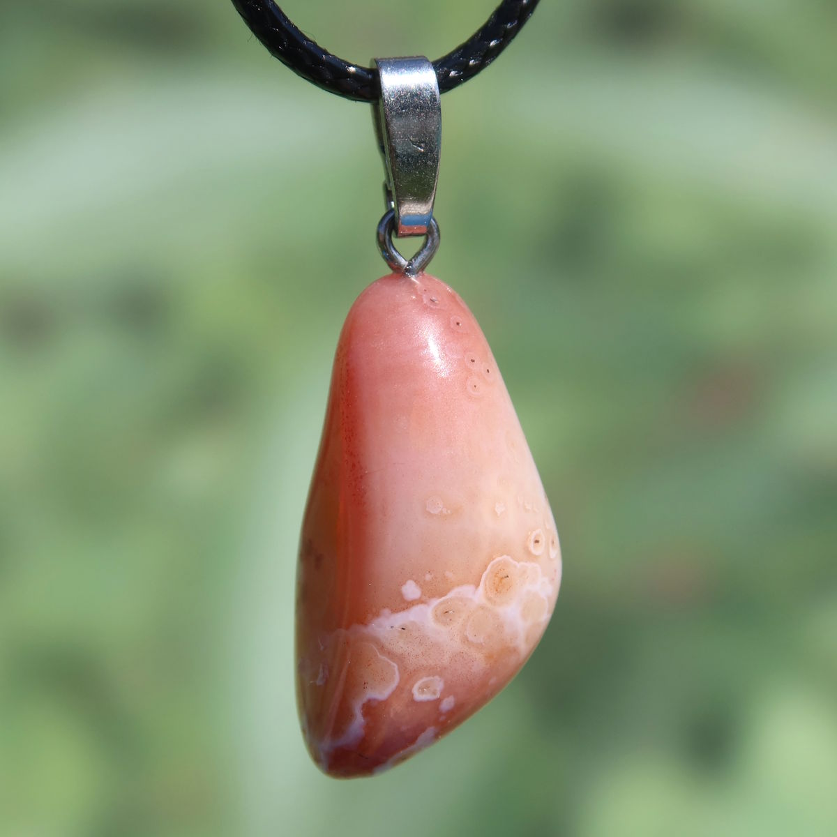 Natürlicher Karneol Anhänger 31mm mit lebendigen Farbstrukturen, UNIKAT Nr. 5, von Steinwelten, vor grünem Hintergrund.