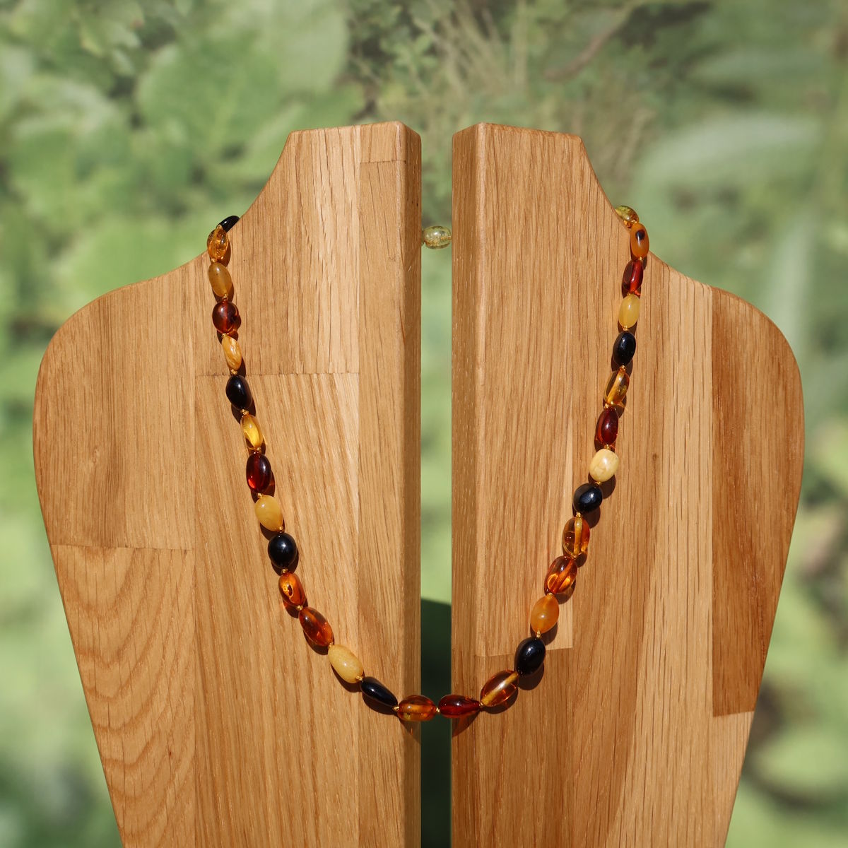 Bernstein Edelsteinkette 45cm auf Holzdisplay vor grünem Hintergrund, edle Kette für Selbstvertrauen und Leichtigkeit.