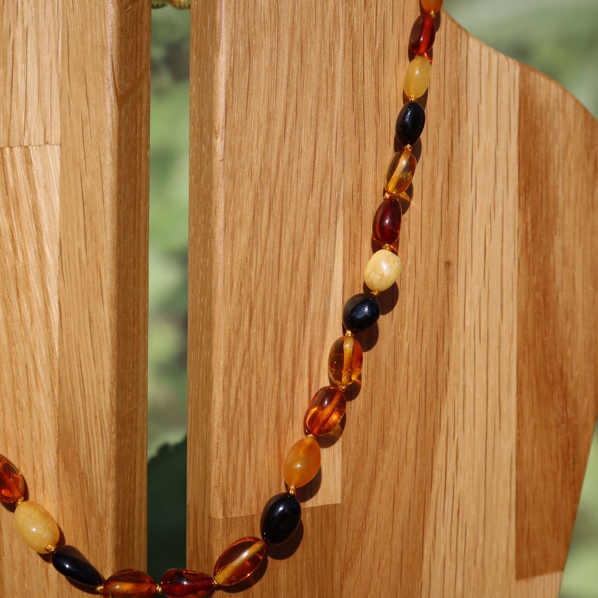 Bernstein Edelsteinkette 45cm auf Holzdisplay vor grünem Hintergrund, edle Kette für Selbstvertrauen und Leichtigkeit.