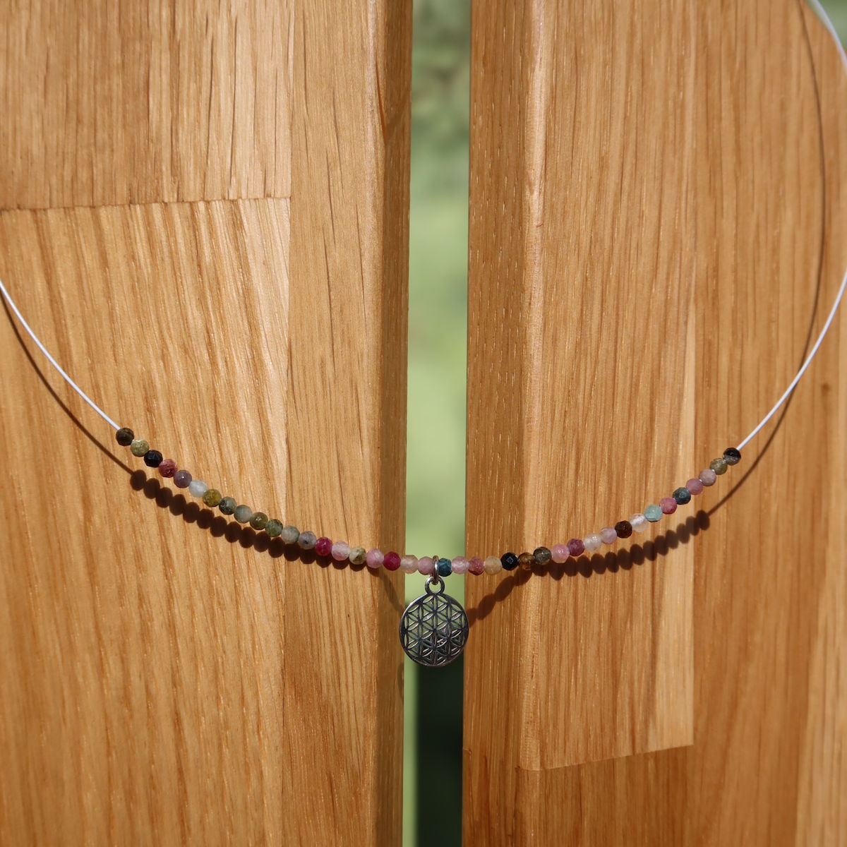 Turmalin bunt Edelsteinkette mit Blume des Lebens in 40cm Länge, für Harmonie und Balance, auf einer Holz-Auslage präsentiert.