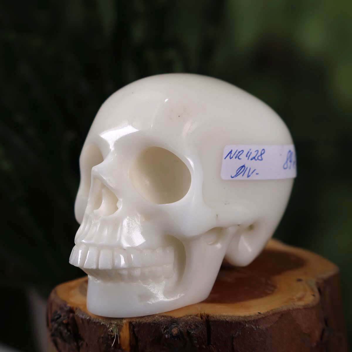 Handcrafted crystal skull made from natural stone, unique design, 7x6 cm, front view on wooden base with blurred green background.