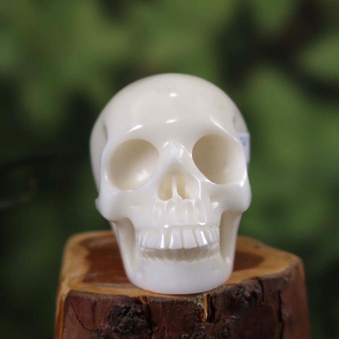 Handcrafted crystal skull made from natural stone, unique design, 7x6 cm, front view on wooden base with blurred green background.