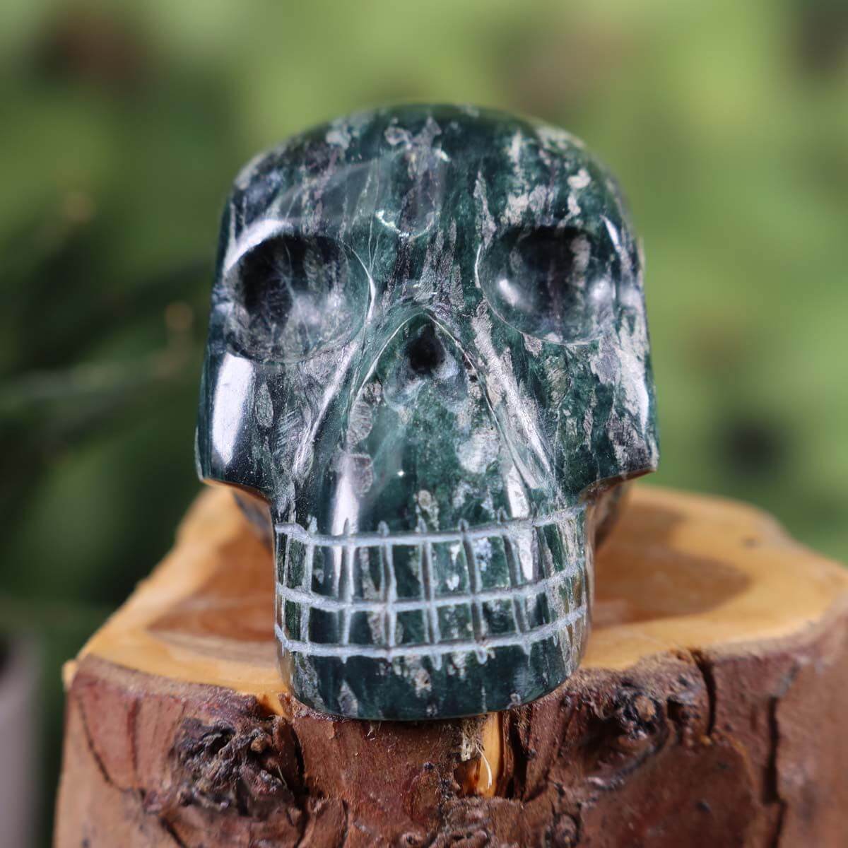 Handcrafted fuchsite crystal skull with unique shape, displayed on wooden base, collectible item, size 6x5 cm.