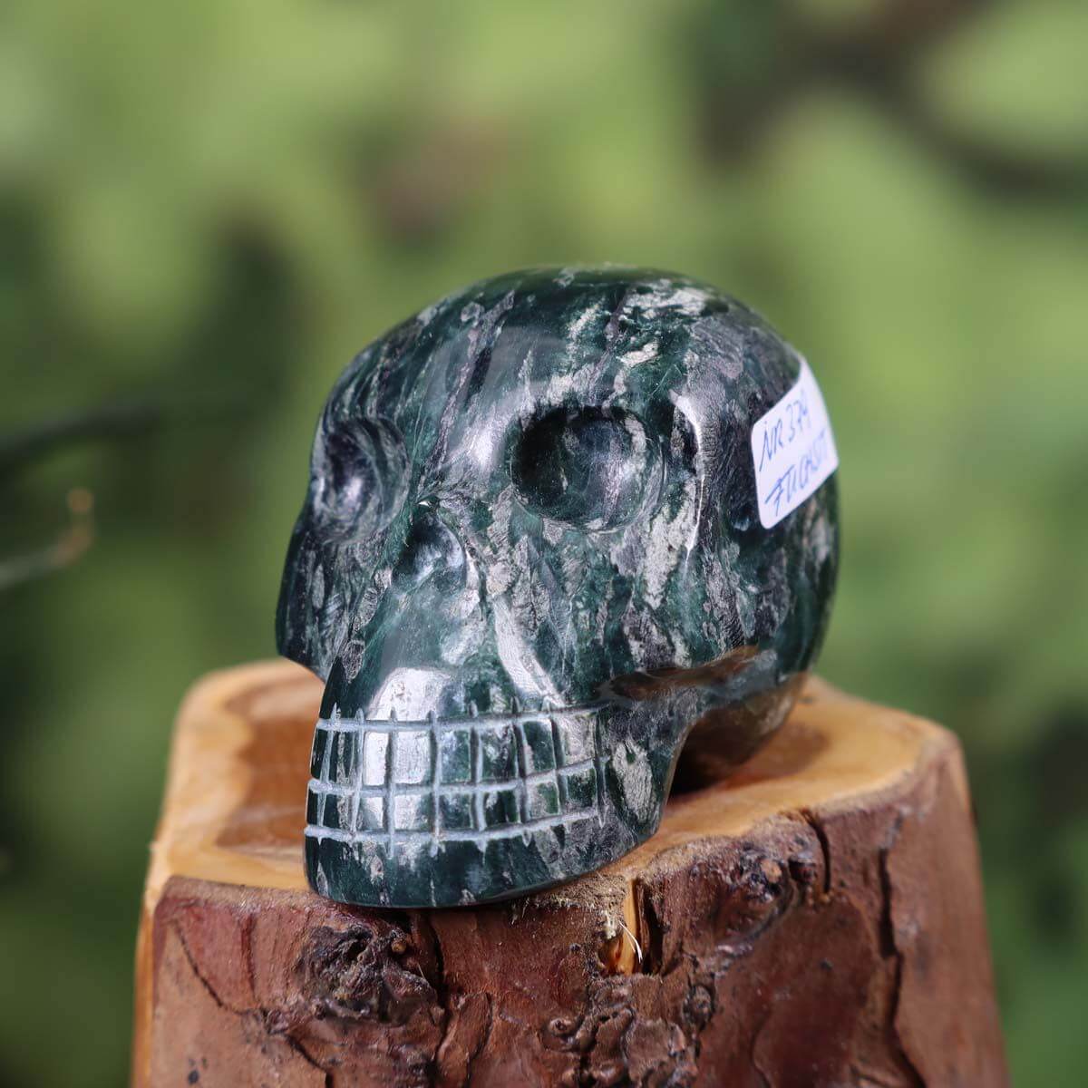 Handcrafted fuchsite crystal skull with unique shape, displayed on wooden base, collectible item, size 6x5 cm.