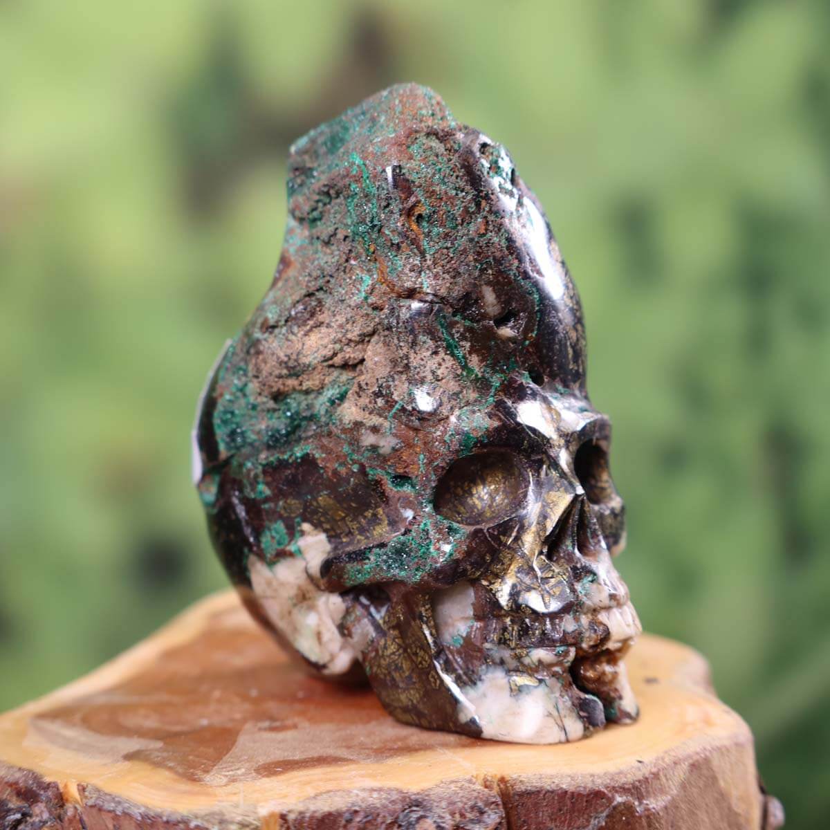 Handcrafted Garnet Uvarovite Crystal Skull on wooden stump, showcasing unique shape and craftsmanship, collectible size 5x6 cm.