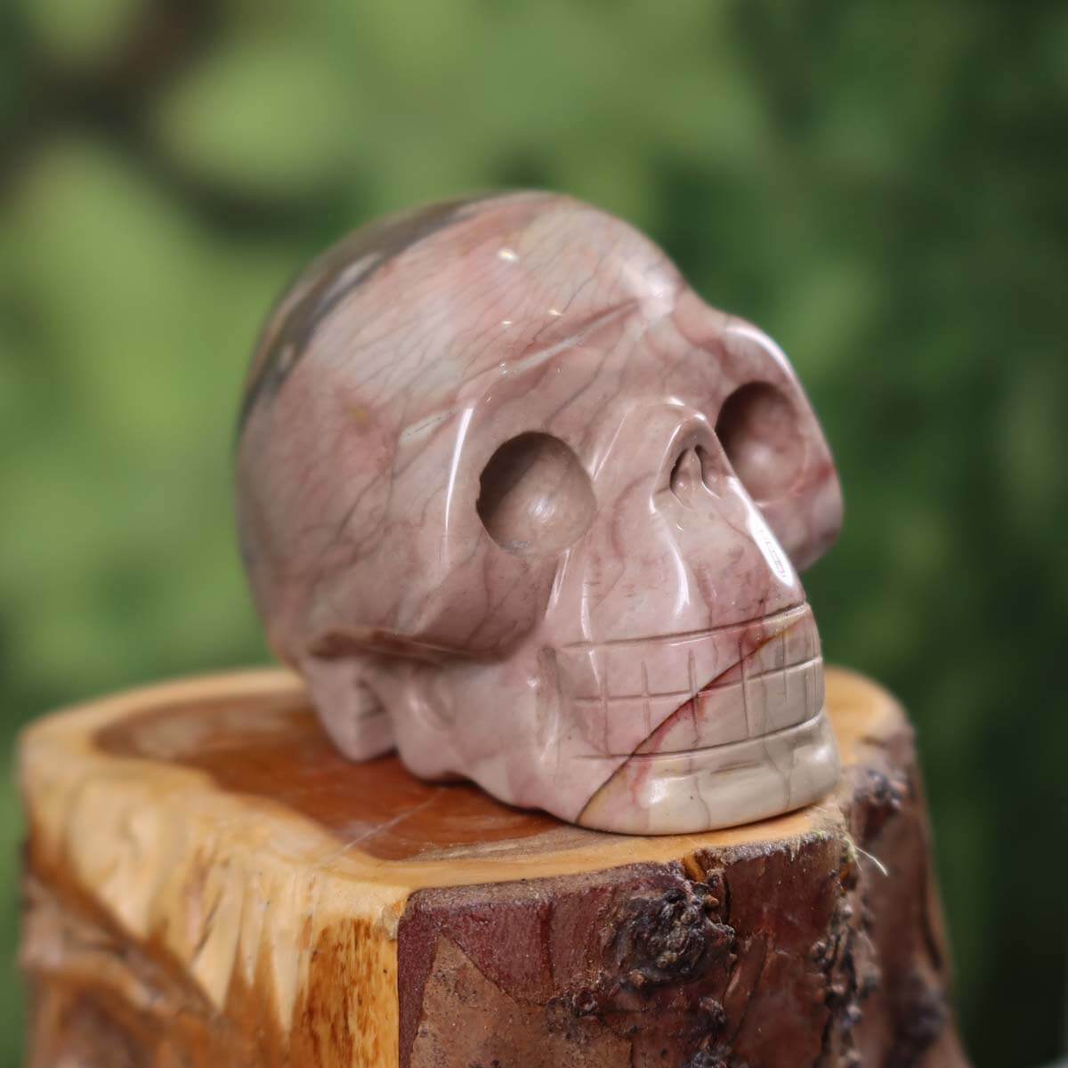 Handcrafted jasper crystal skull with unique coloration on wooden base, collector's item, 7x5 cm.