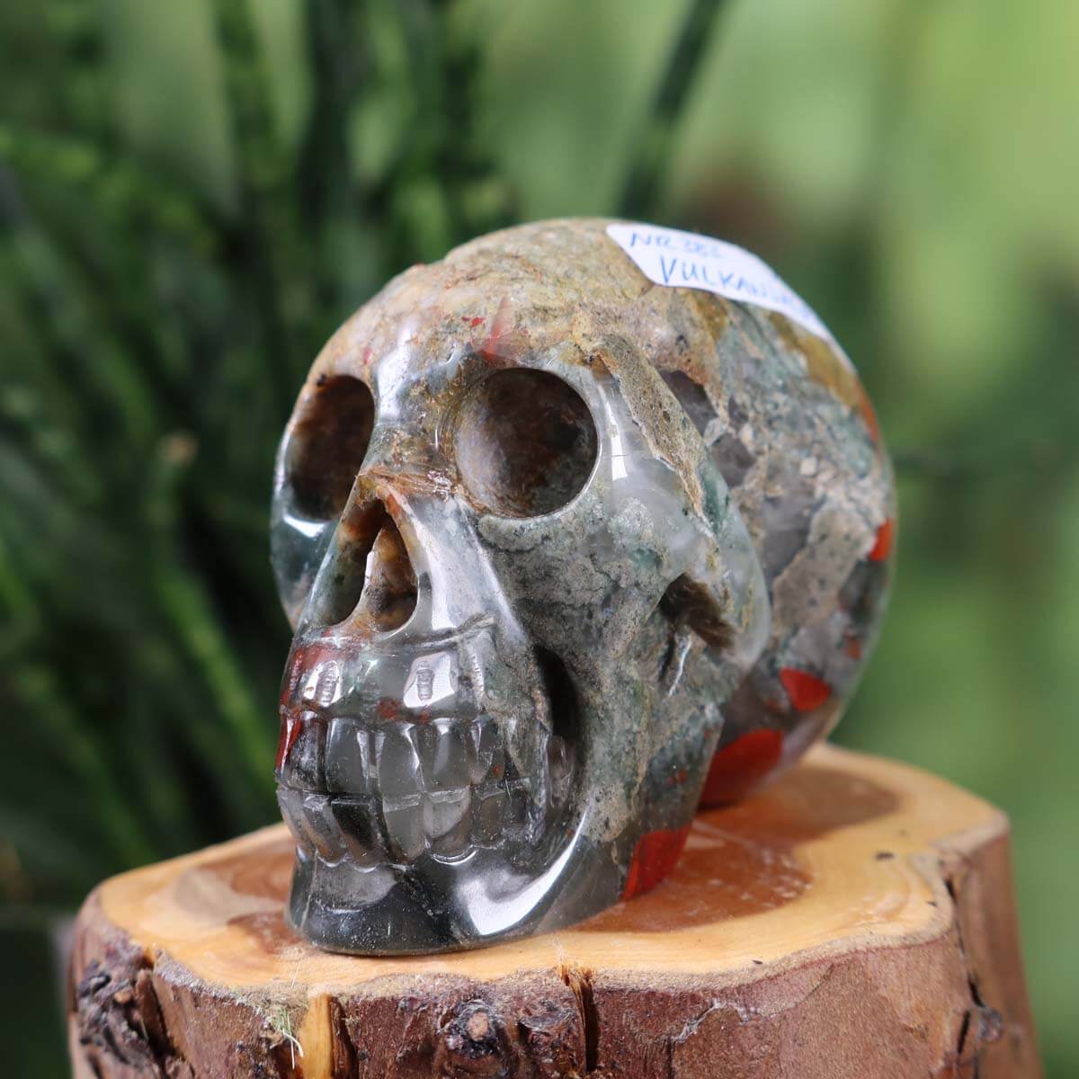 Handcrafted volcanic jasper crystal skull sculpture, unique collector's item with intricate details, set on a wooden base.