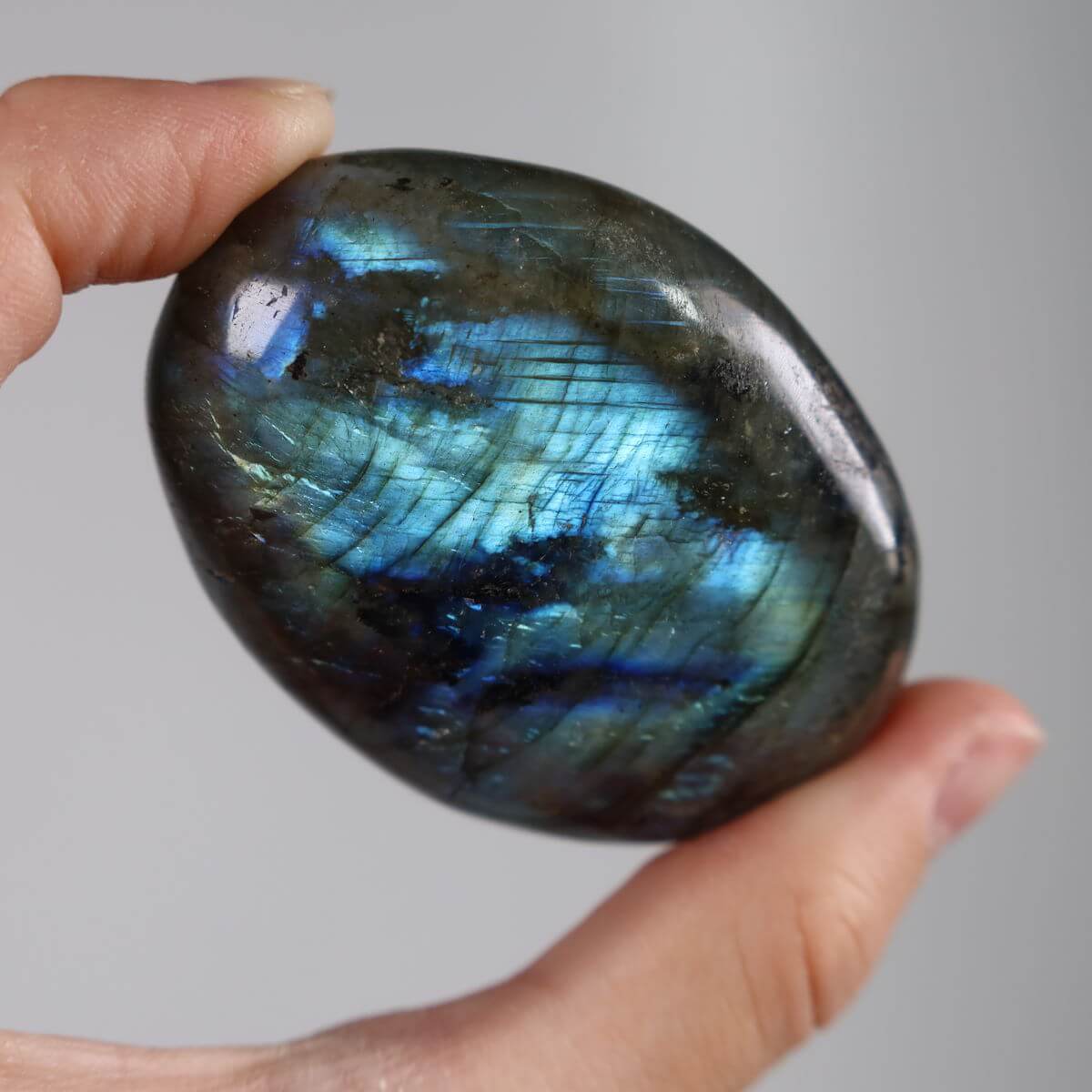 Hand holding two polished Labradorite palm stones with vibrant blue and green hues, ideal for relaxation and creativity enhancement.