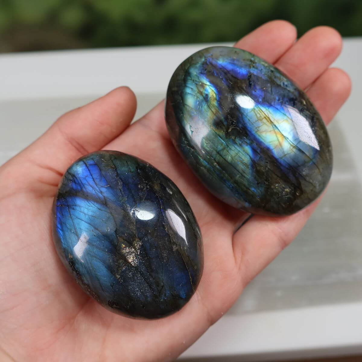 Hand holding two polished Labradorite palm stones with vibrant blue and green hues, ideal for relaxation and creativity enhancement.