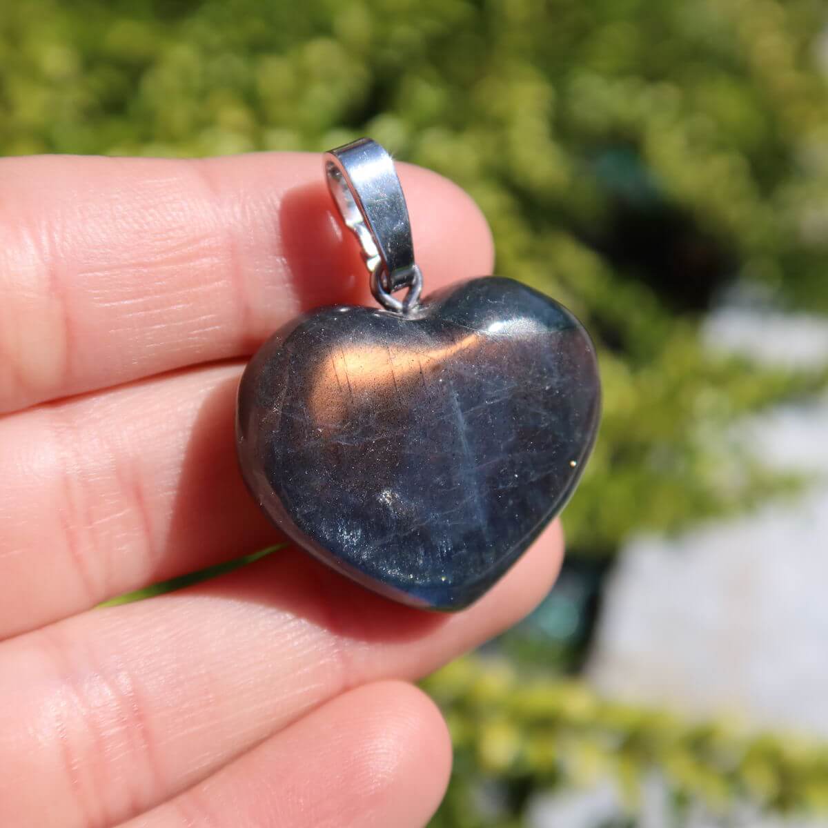 Heart-shaped labradorite pendant with a glowing brown sheen against a blurred green background.
