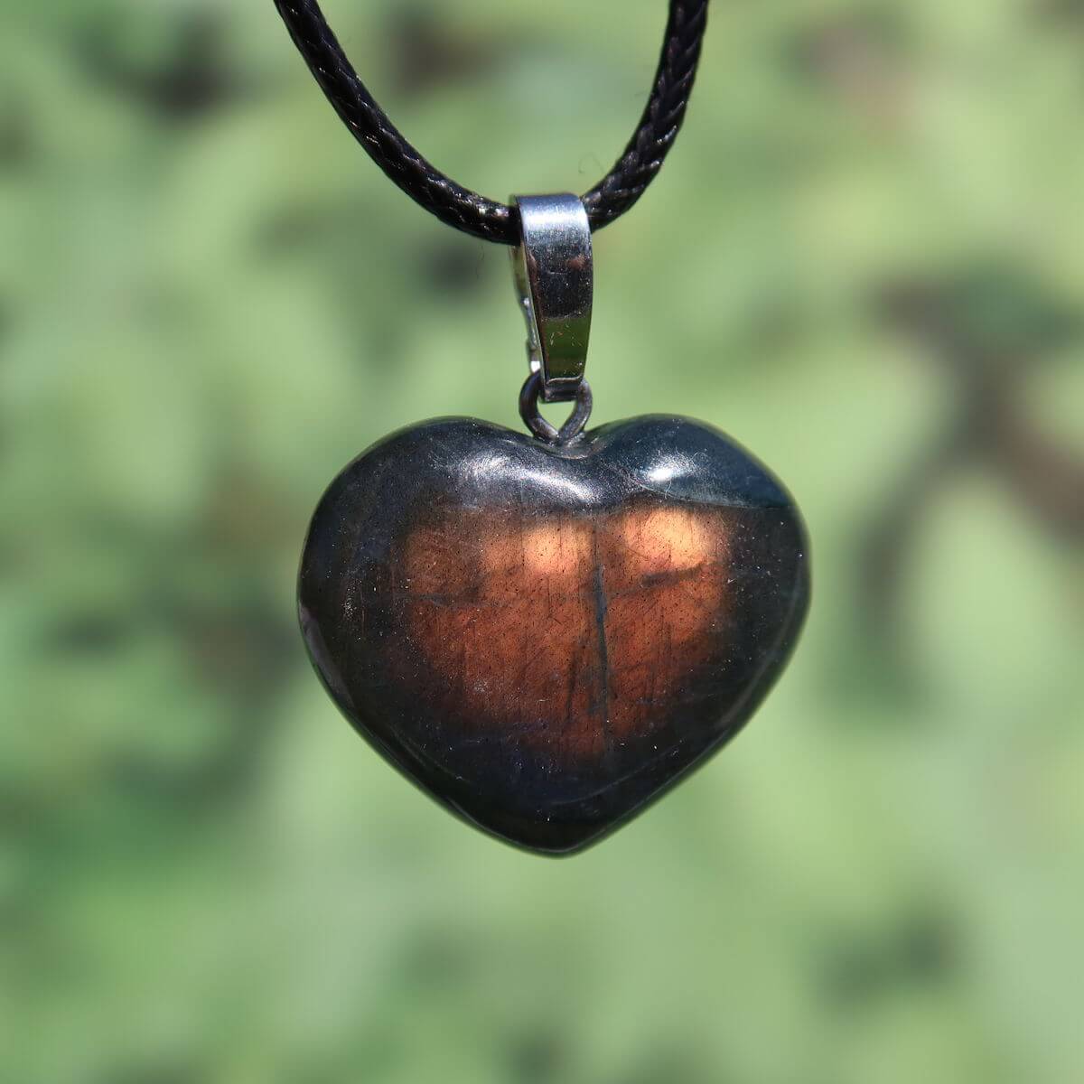 Heart-shaped labradorite pendant with a glowing brown sheen against a blurred green background.