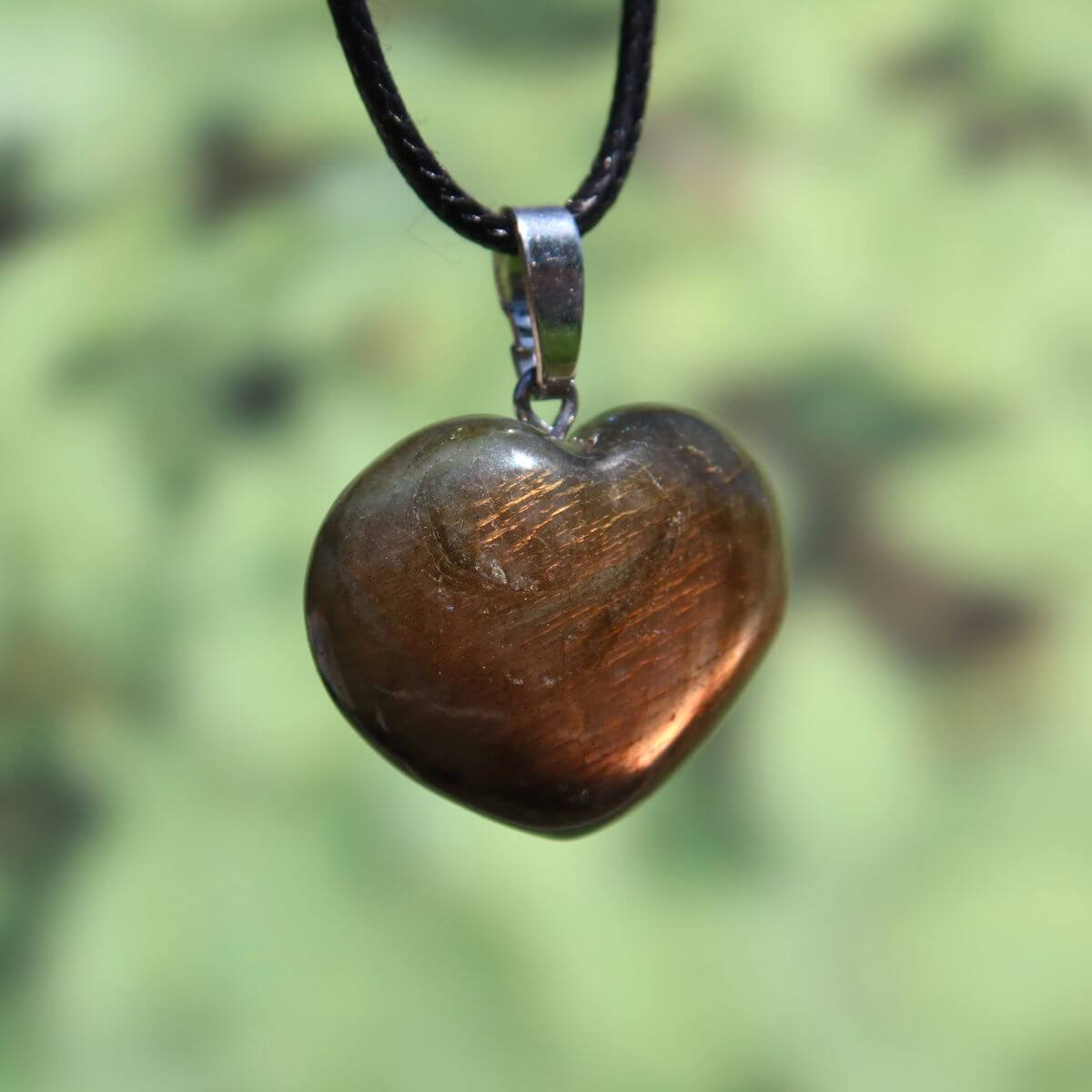 Heart-shaped Labradorite pendant with shimmering hues on black cord, showcasing unique colors under light.