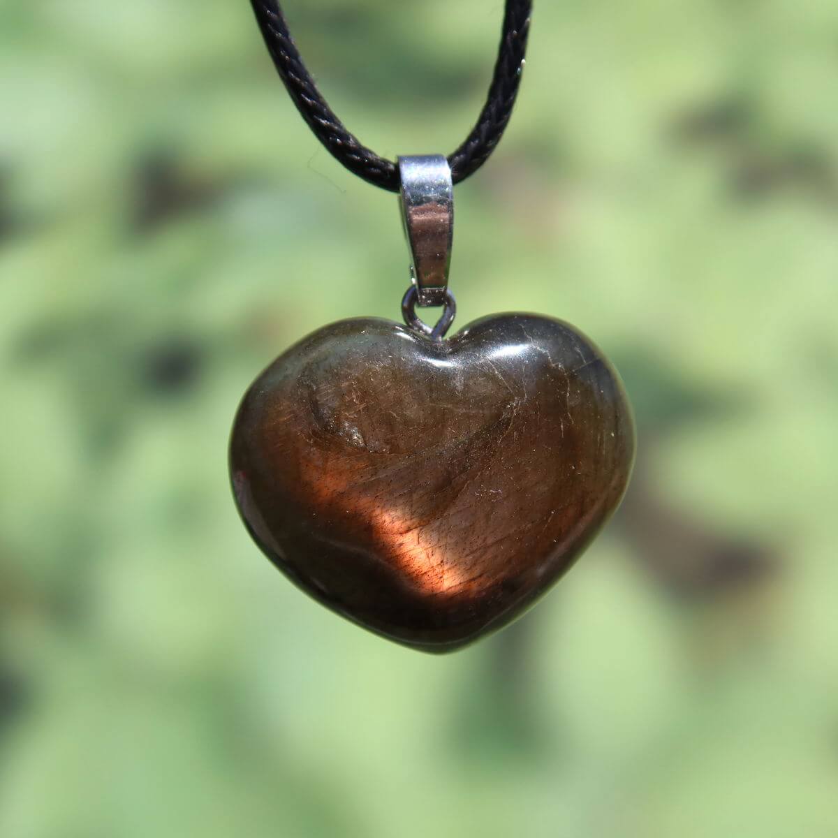 Heart-shaped Labradorite pendant with shimmering hues on black cord, showcasing unique colors under light.