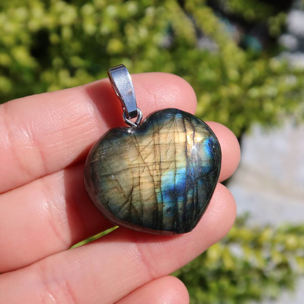 Heart-shaped Labradorite pendant in a hand, showcasing blue, green, and gold hues with a vibrant sheen, emphasizing spirituality.