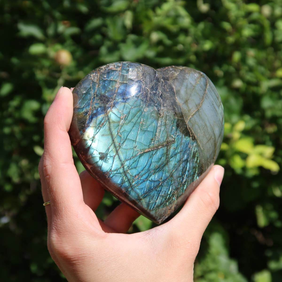 Hand holding a large Labradorite heart gemstone, displaying a unique blue-green color play.
