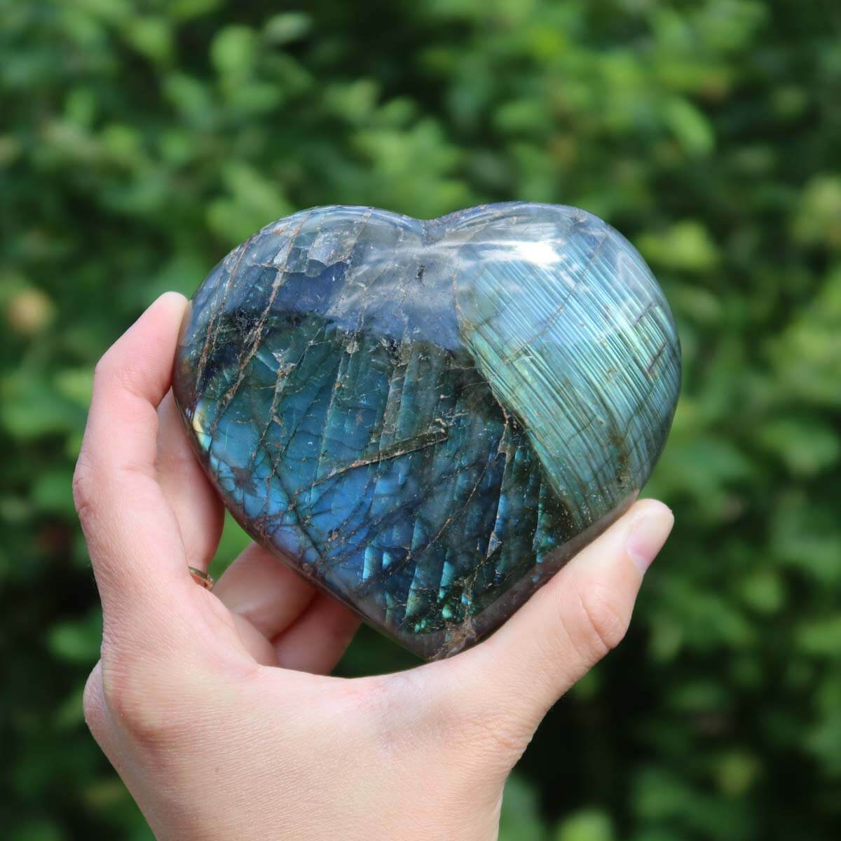 Hand holding a large Labradorite heart gemstone, displaying a unique blue-green color play.