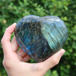 Hand holding large labradorite heart stone with blue and green shimmer, unique gemstone for relaxation and creativity boosting.