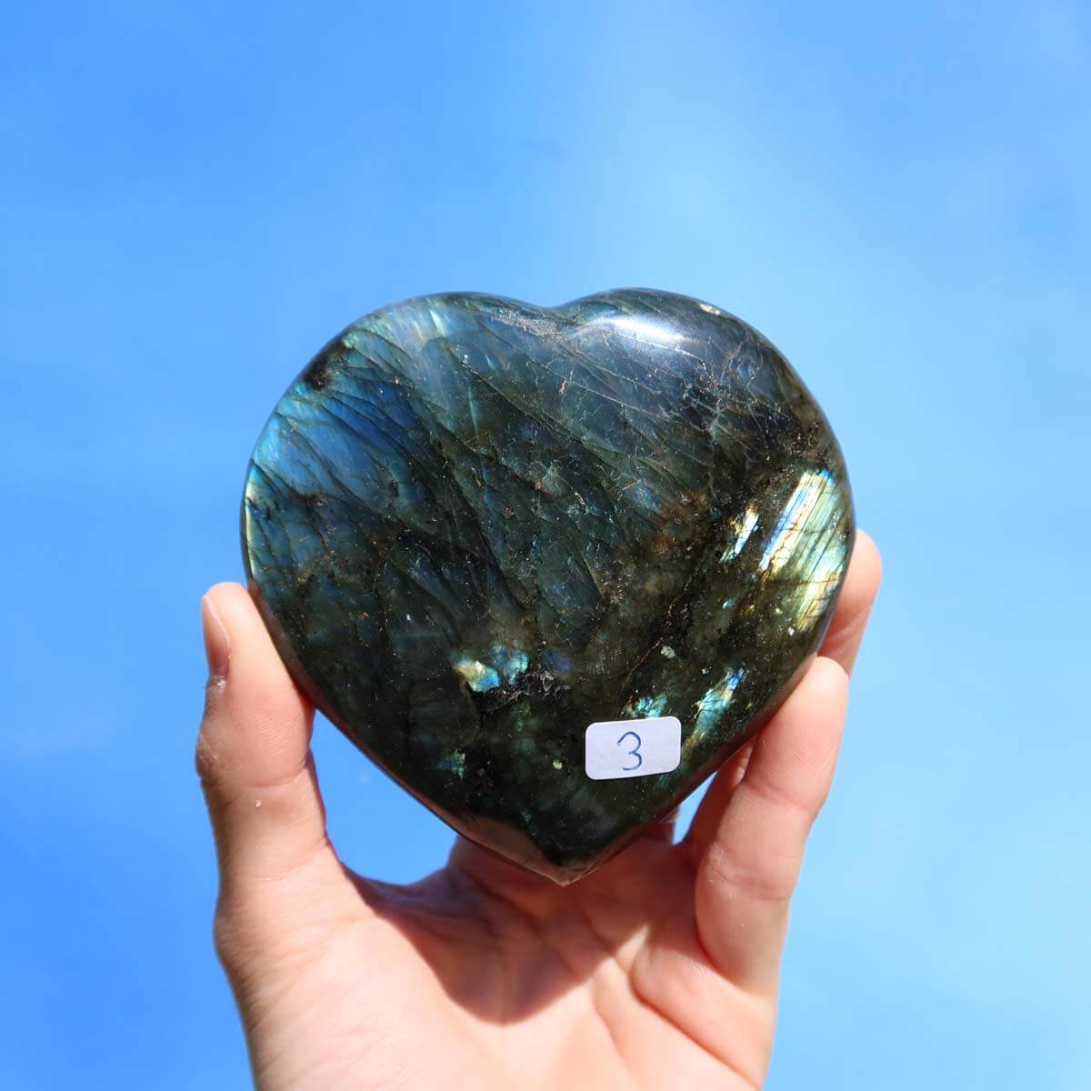 Großes Labradorit Herz Edelstein Unikat zur Entspannung und Kreativität, handgehalten vor blauem Hintergrund