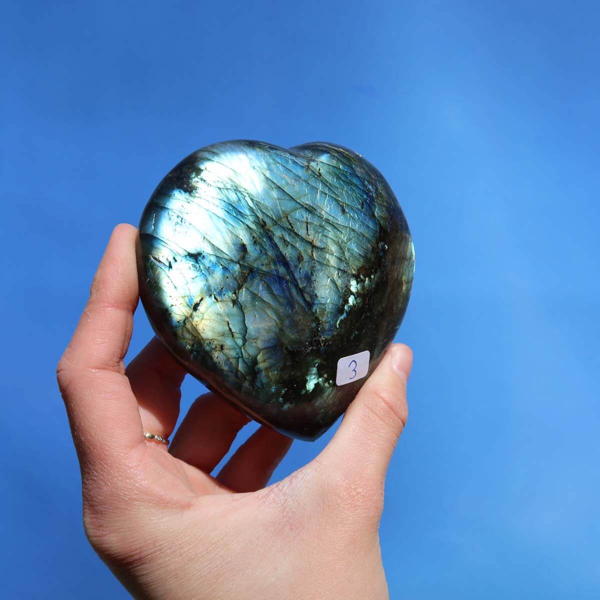 Großes Labradorit Herz Edelstein Unikat zur Entspannung und Kreativität, handgehalten vor blauem Hintergrund