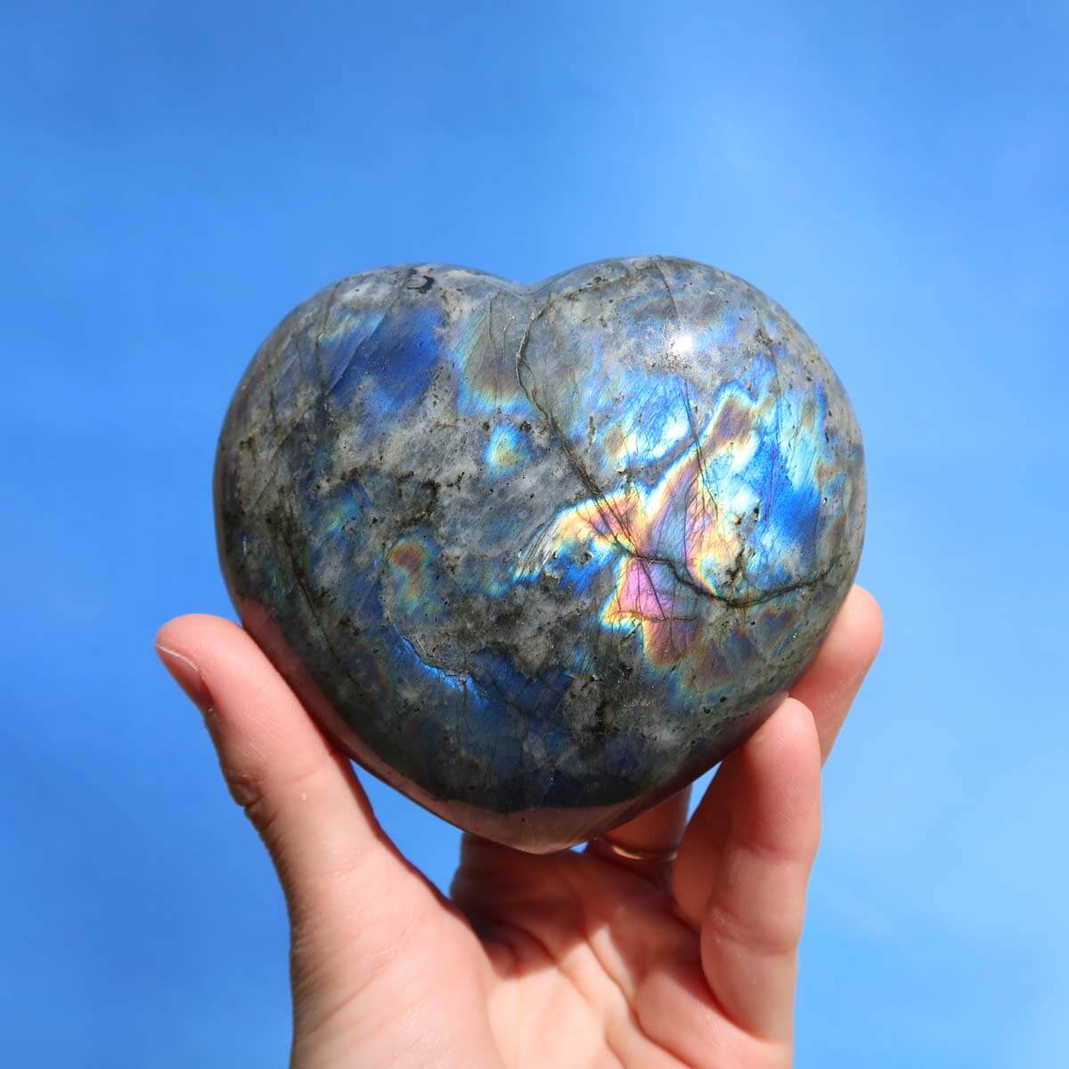 Labradorite heart gemstone with iridescent colors, held in hand, against a blue background