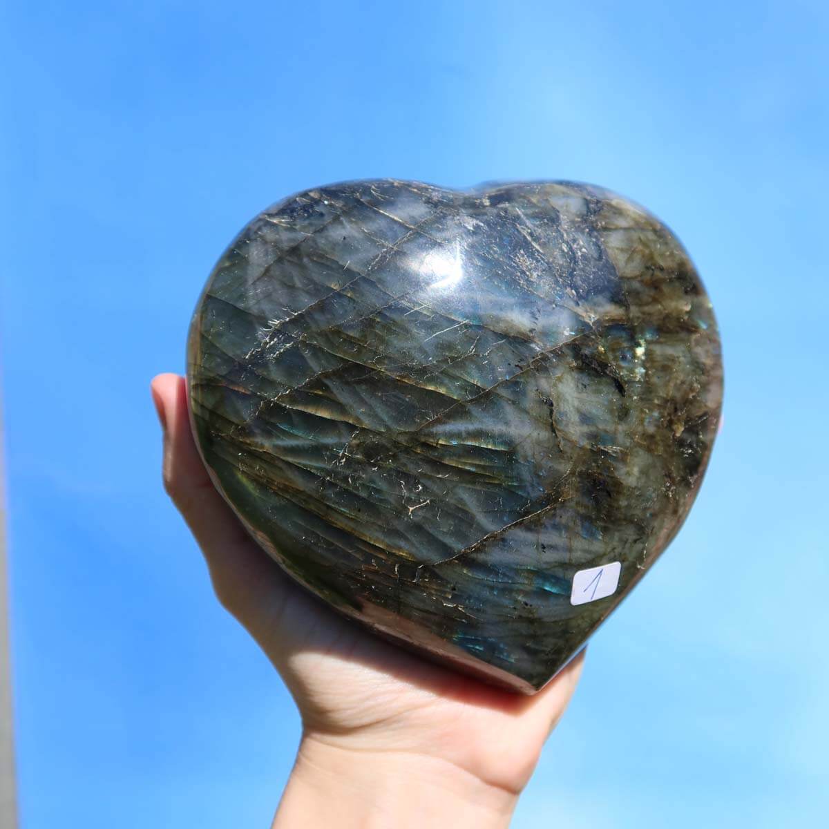 Hand holding large Labradorit gem heart with vibrant blue, green, and gold hues, unique texture, and polished finish for creativity boost.