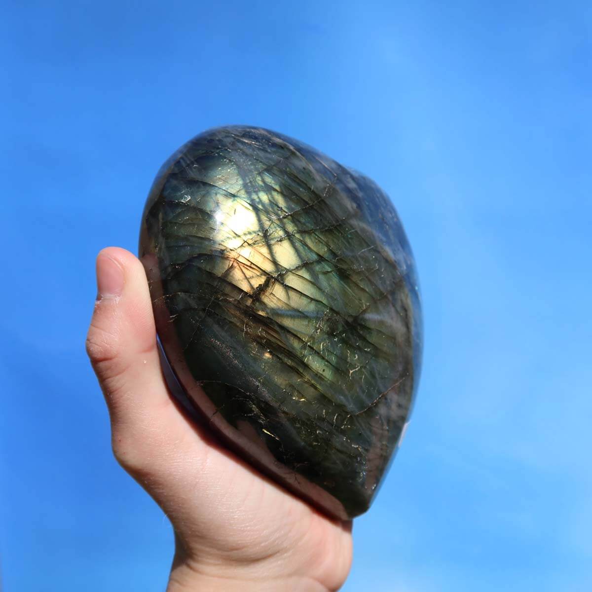 Hand holding large Labradorit gem heart with vibrant blue, green, and gold hues, unique texture, and polished finish for creativity boost.