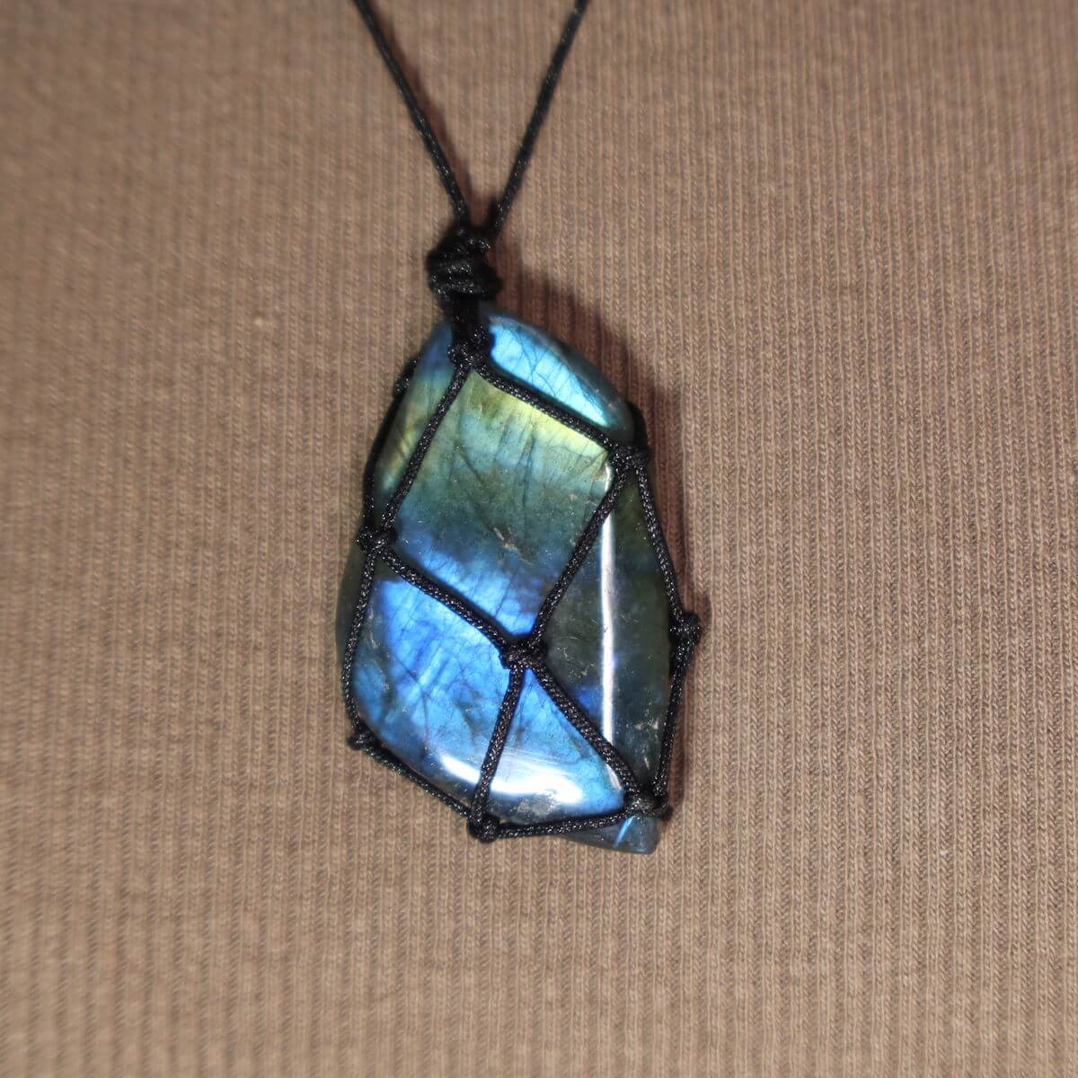 Labradorit Anhänger mit handgefertigter Makramee Kette, längenverstellbar und einzigartig, Naturstein vor unscharfem Hintergrund