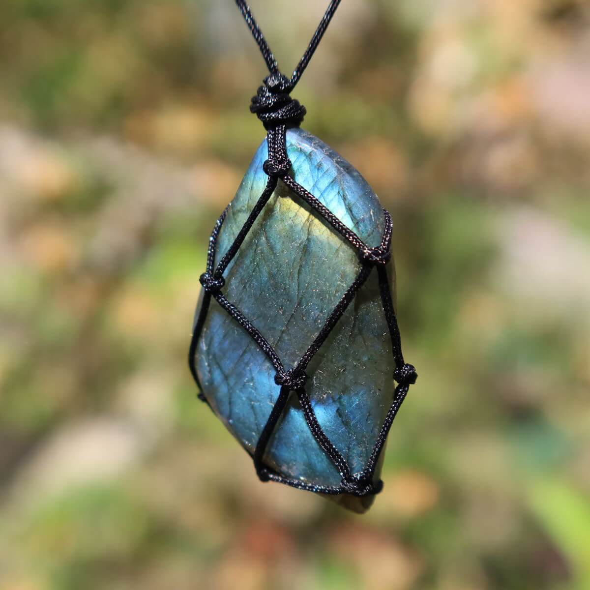 Labradorit Anhänger mit handgefertigter Makramee Kette, längenverstellbar und einzigartig, Naturstein vor unscharfem Hintergrund