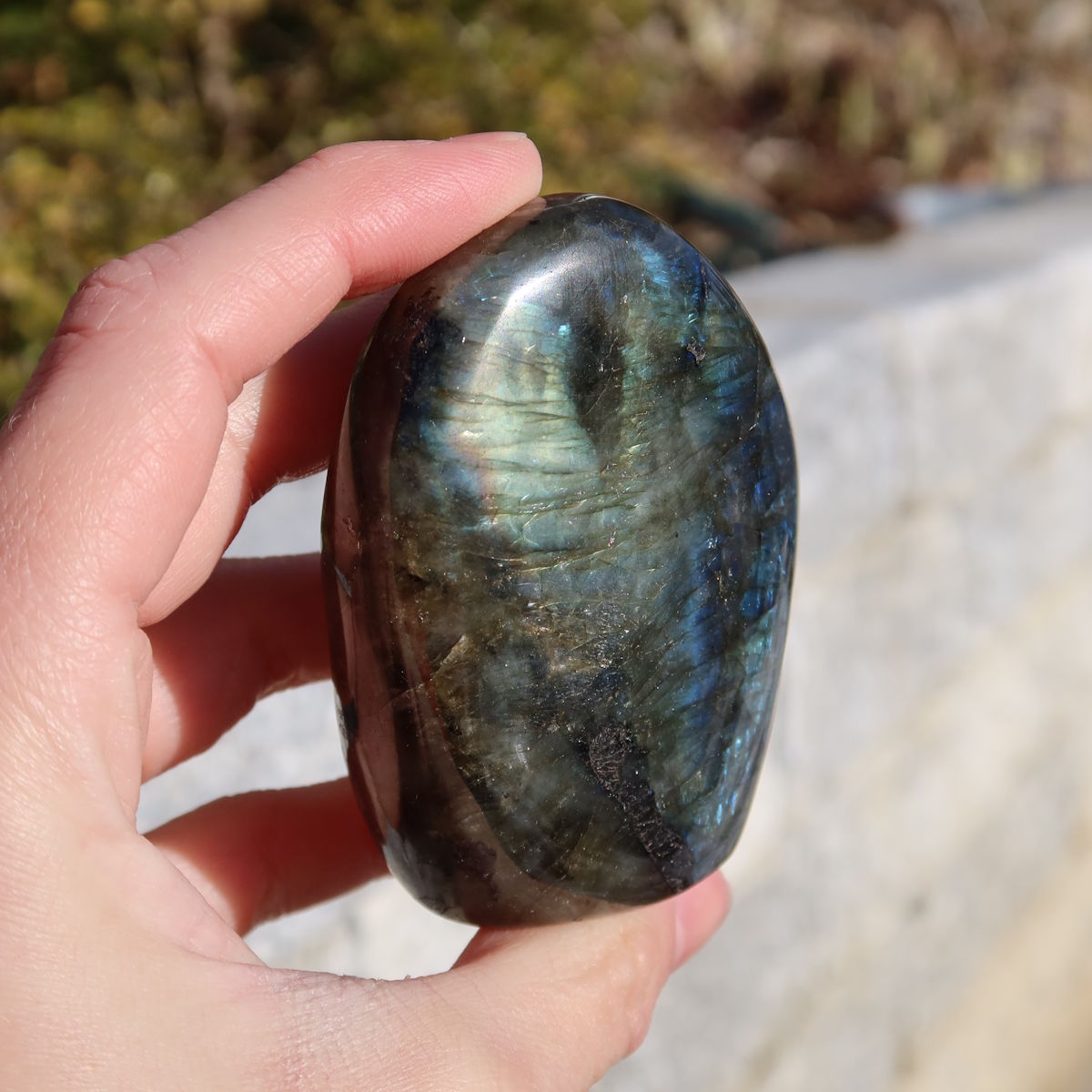 Labradorit Freiform poliert - 7x5cm - Intuition und Kreativität Nr.14 in der Hand gehalten, zeigt faszinierende Labradoreszenz.